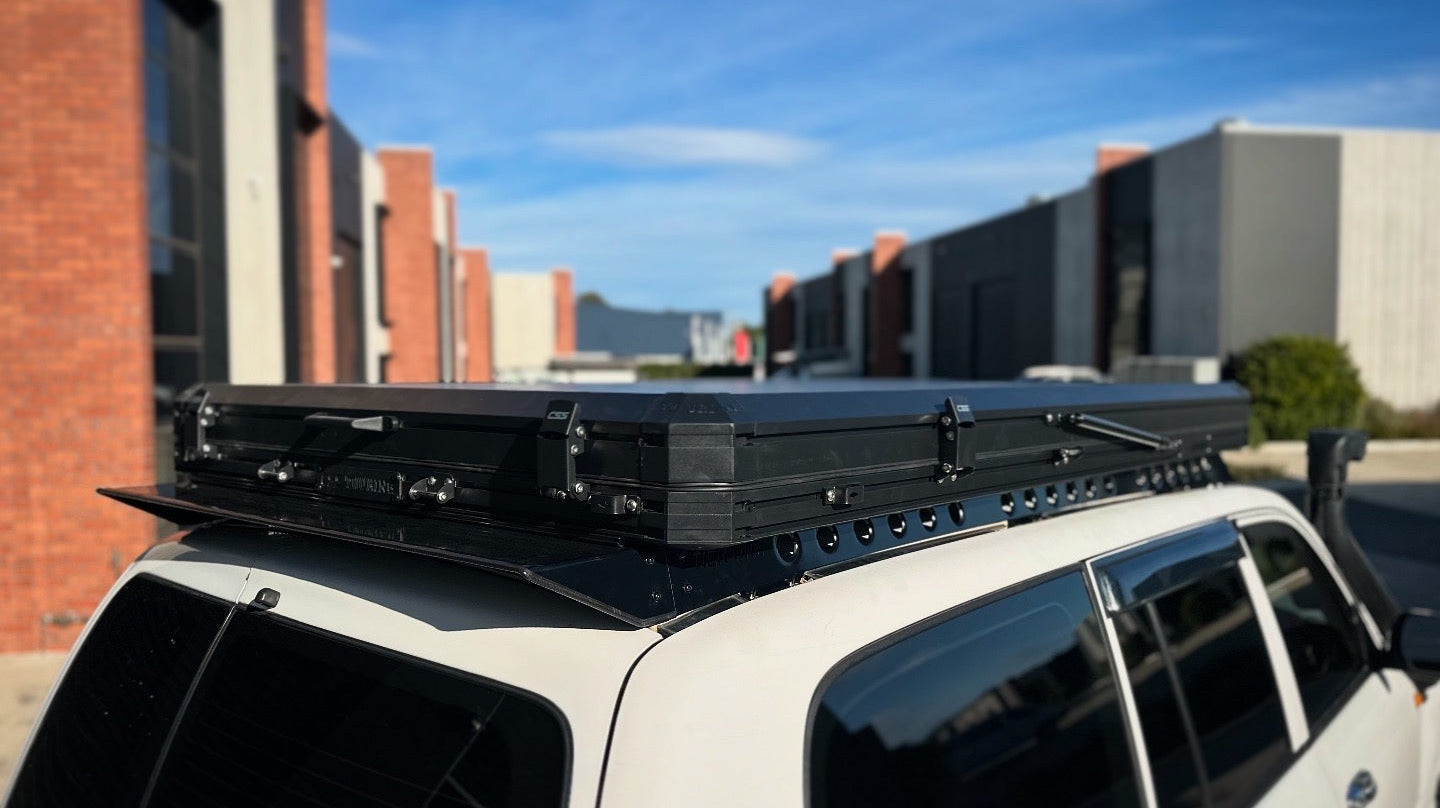 This is an image of a white 4x4 fitted with a black Tier One Metalworks Roof Rack & Rails under a closed rooftop tent in an industrial area