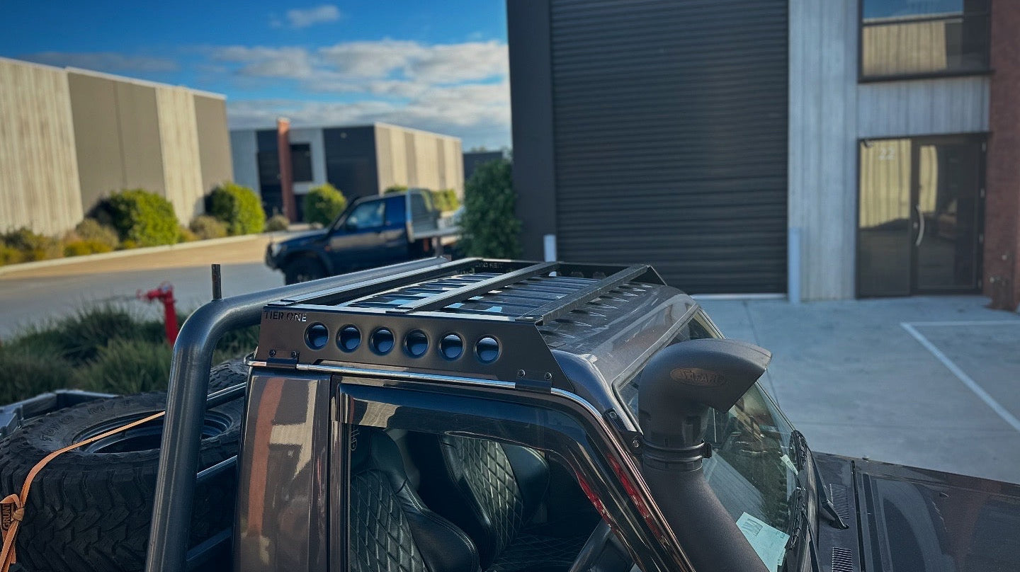 This is an image of a black Nissan Patrol GXL featuring a Tier One Metalworks black roof rack and snorkel in an industrial area