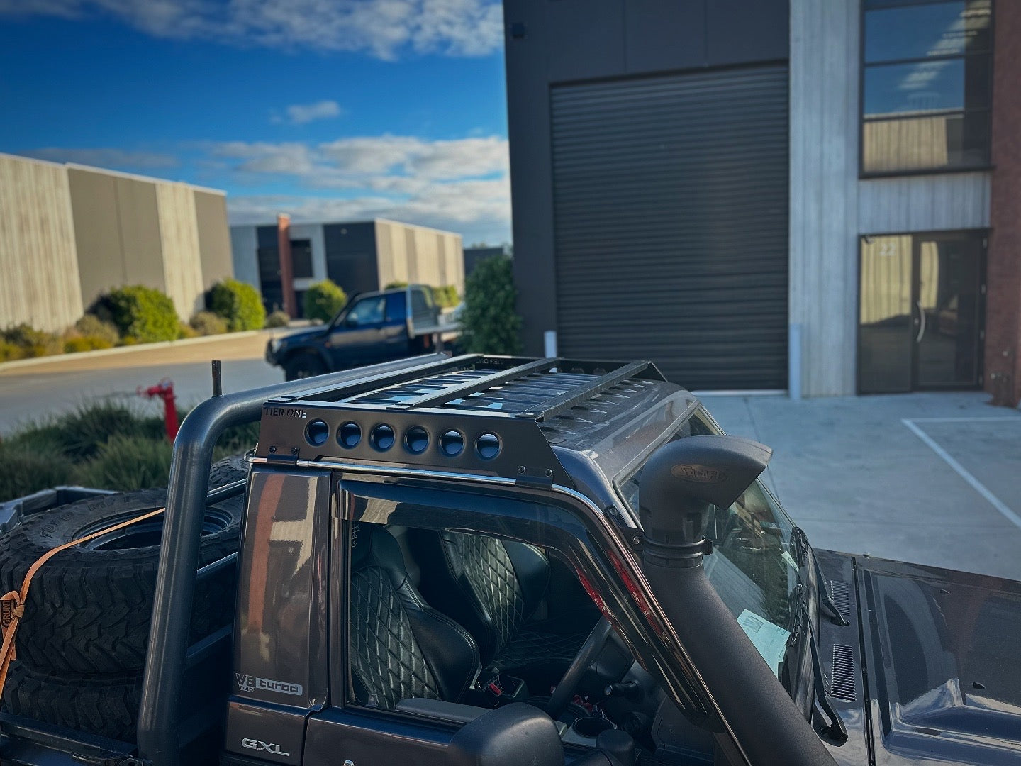 This is an image of a black Nissan Patrol GXL featuring a Tier One Metalworks black roof rack and snorkel in an industrial area
