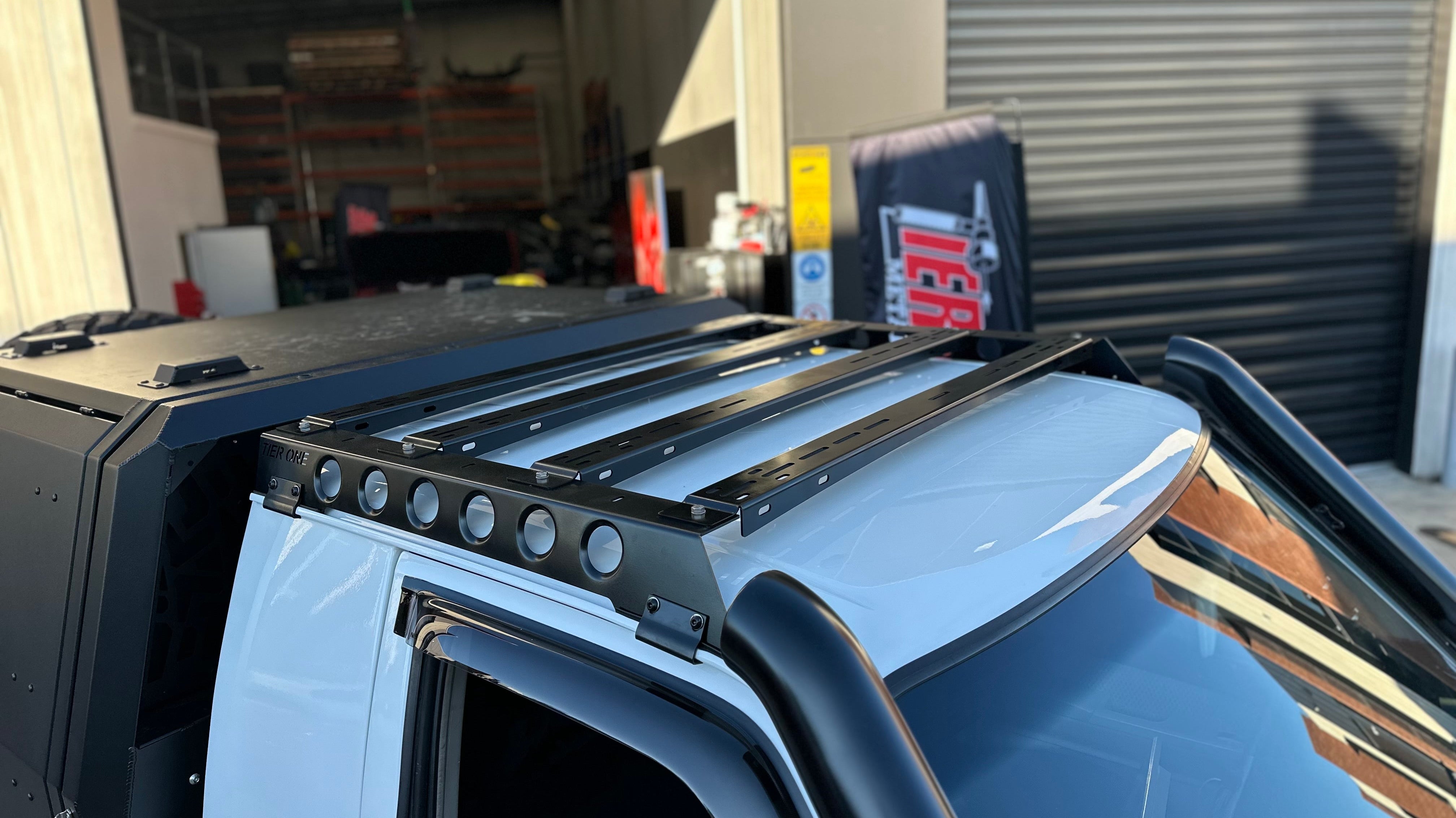 This is an image of a white 4x4 with Tier One Metalworks Roof Racks & Rails installed on the roof in a workshop setting