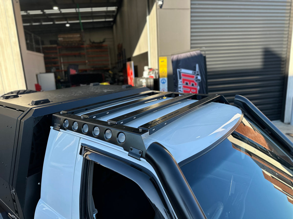 This is an image of a white 4x4 with Tier One Metalworks Roof Racks & Rails installed on the roof in a workshop setting