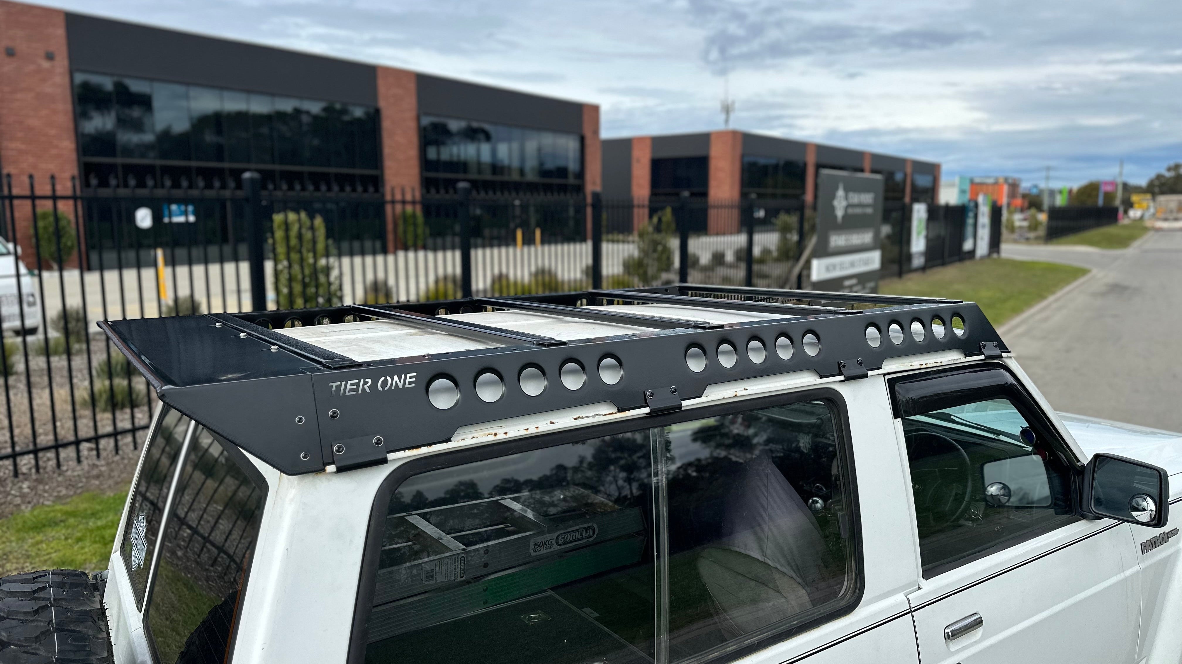 This is an image of a white Nissan Patrol fitted with a black Tier One Metalworks Roof Rack on an urban street.