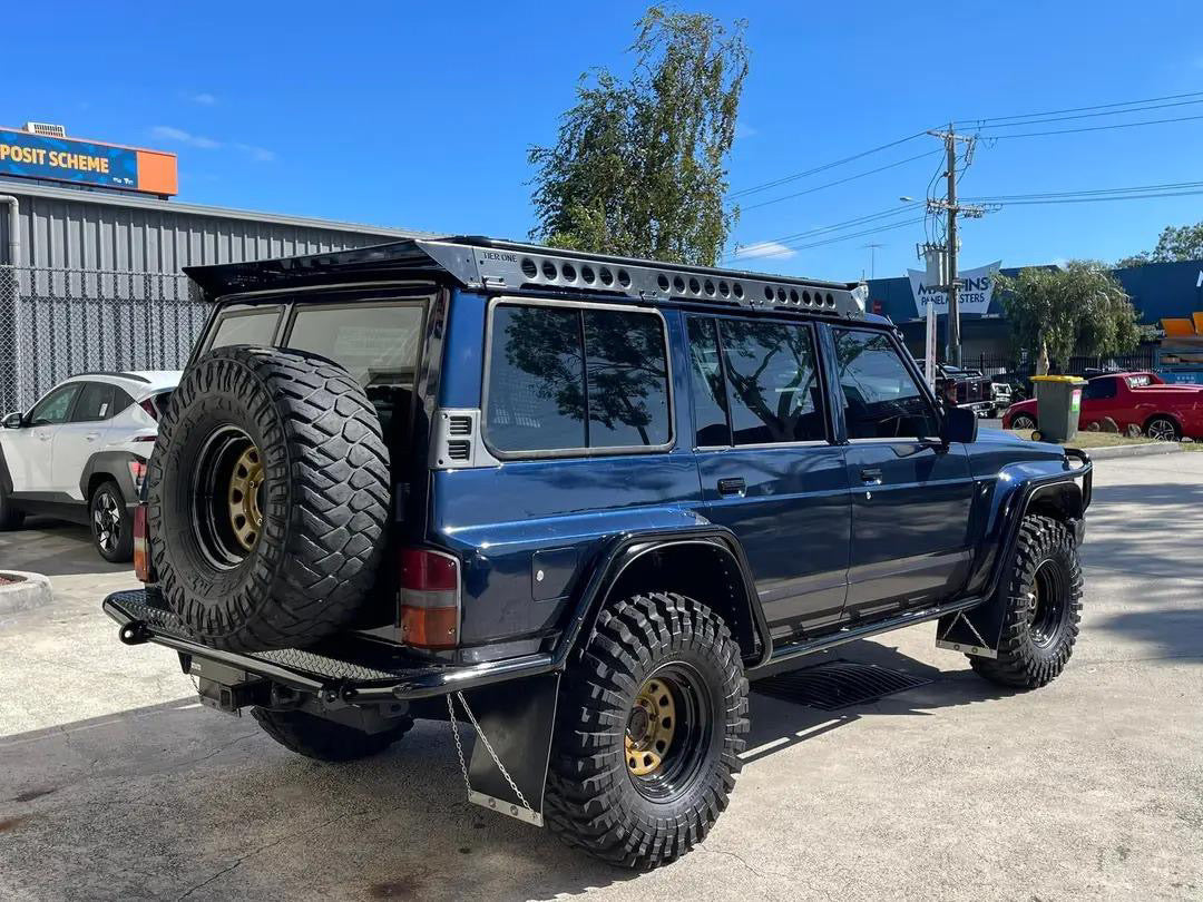This is an image of a blue Nissan Patrol 4WD with Tier One Metalworks roof racks and rails, off-road tyres and rear spare wheel.