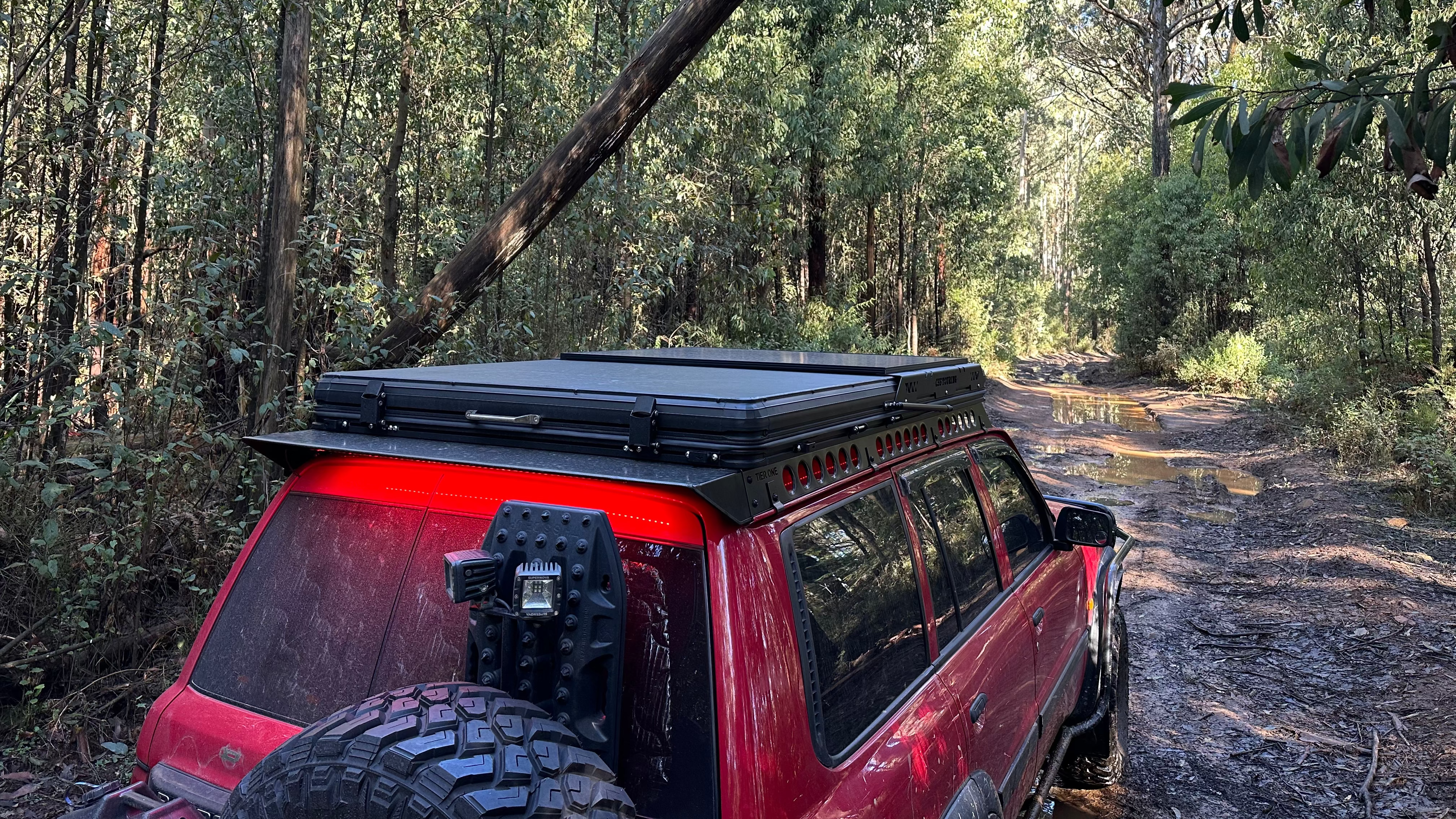 This is an image of a red Nissan Patrol with a Tier One Metalworks roof rack and rails, off-road in Australian bushland