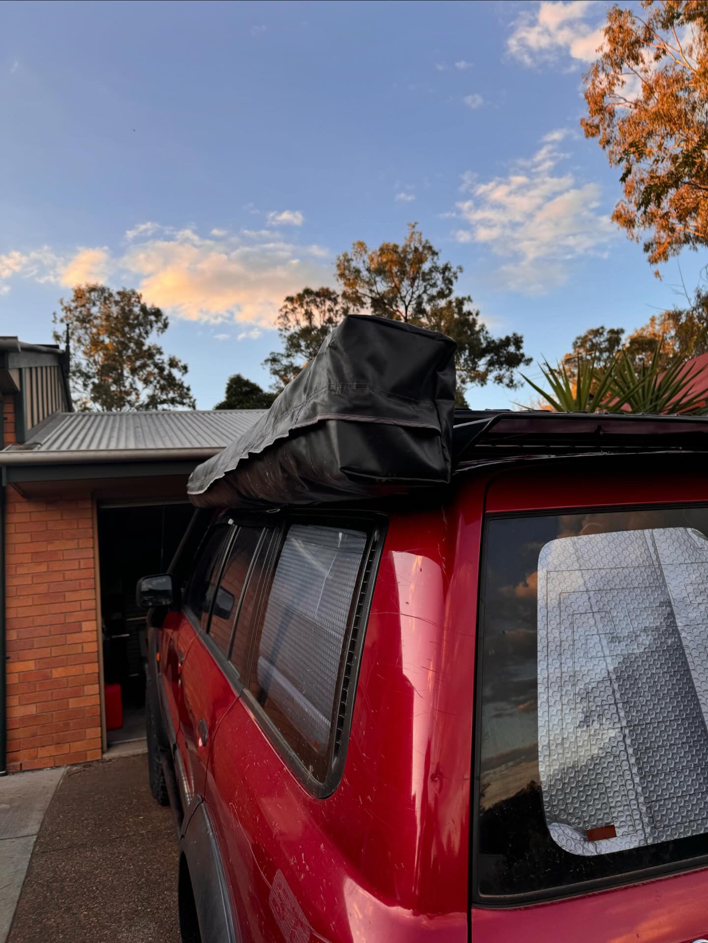 This is an image of a red 4WD with a black rooftop tent mounted on Tier One Metalworks roof racks in a residential driveway