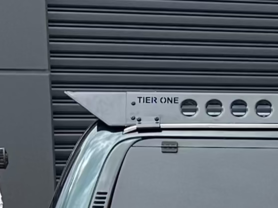 This is an image of a silver Tier One Metalworks roof rack mounted on a dark vehicle with a black roller door background