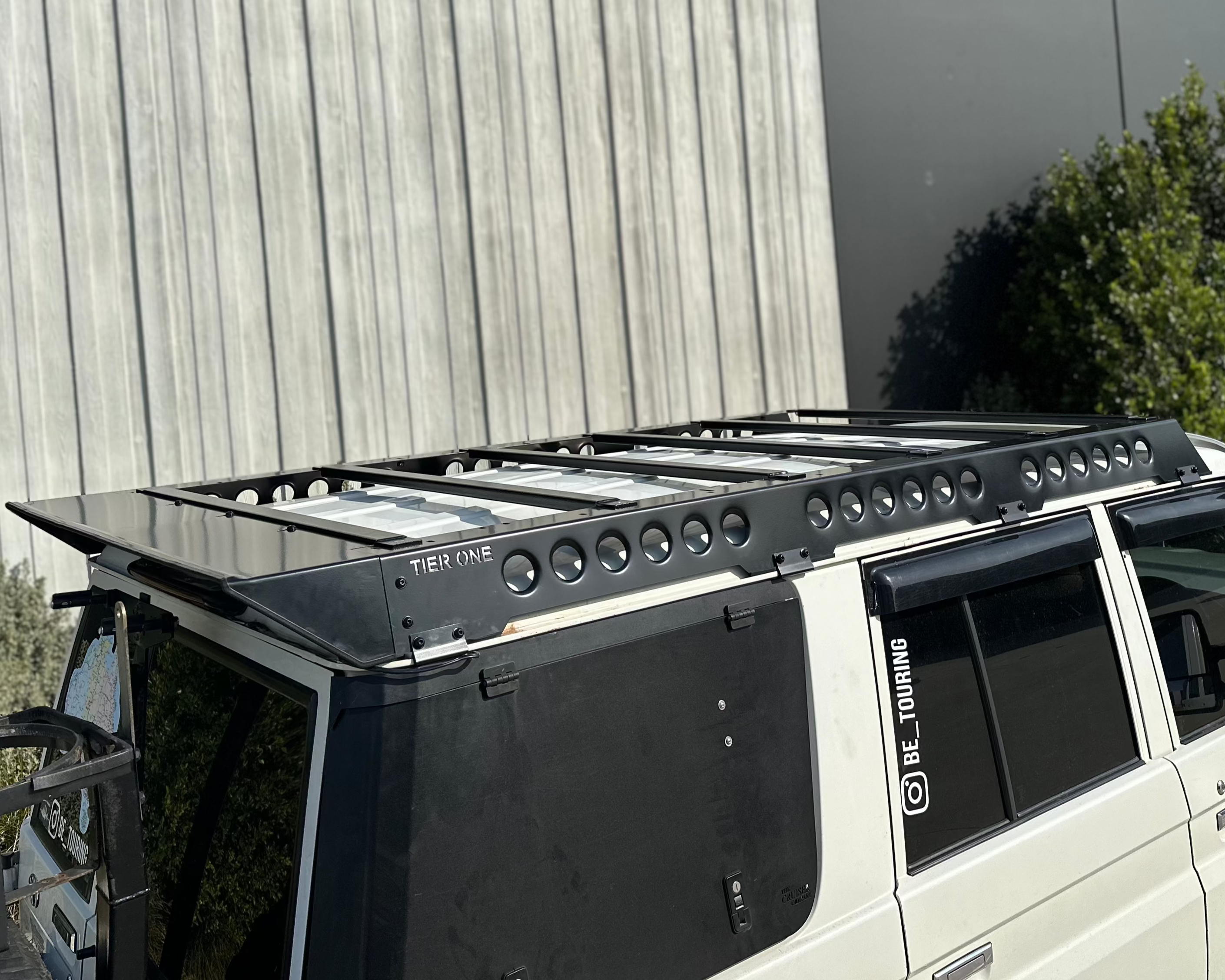 This is an image of a white 4WD fitted with a black Tier One Metalworks roof rack and rails on the vehicle roof