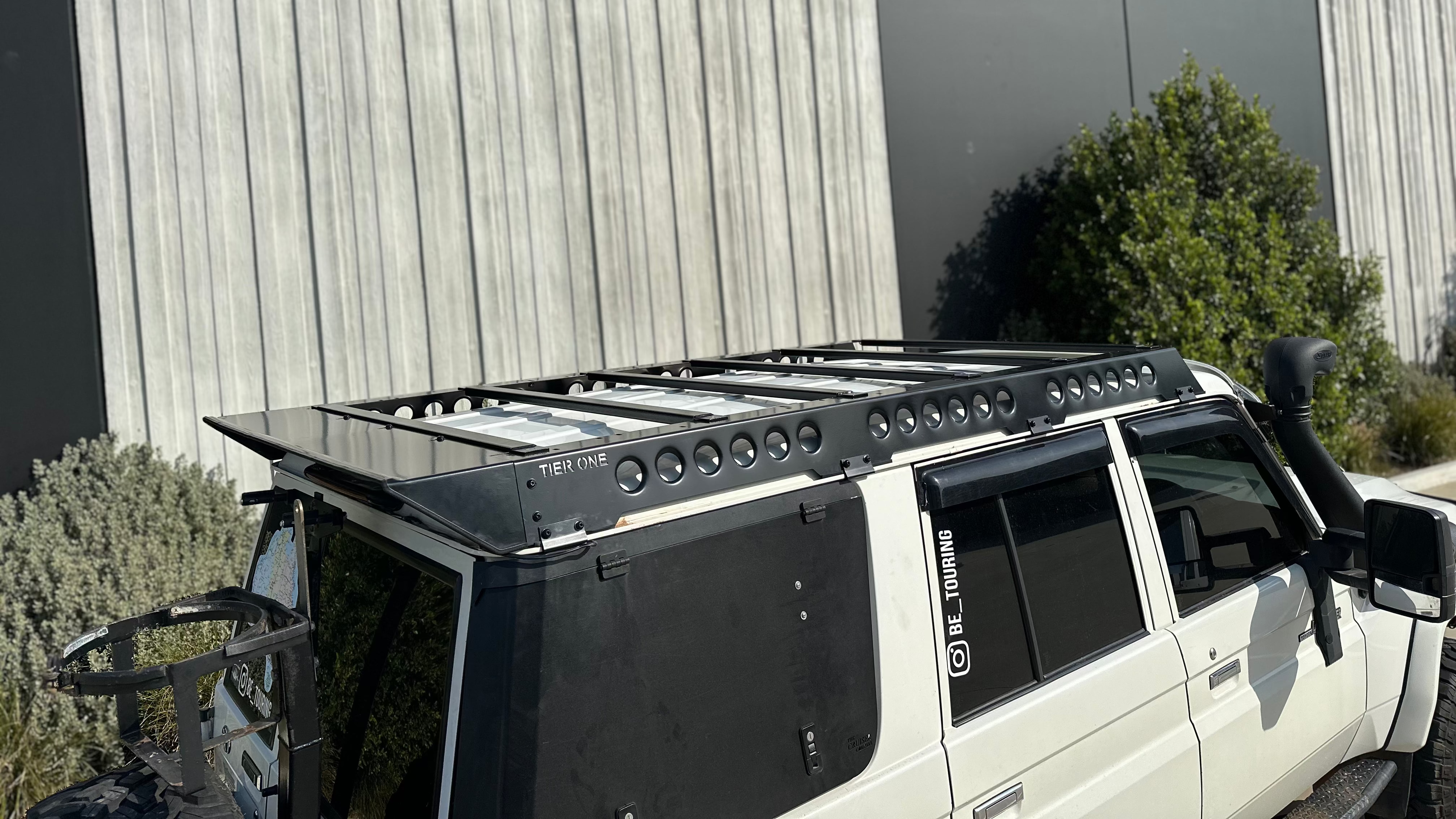 This is an image of a white 4x4 vehicle featuring a black Tier One Metalworks roof rack and snorkel in an outdoor setting.
