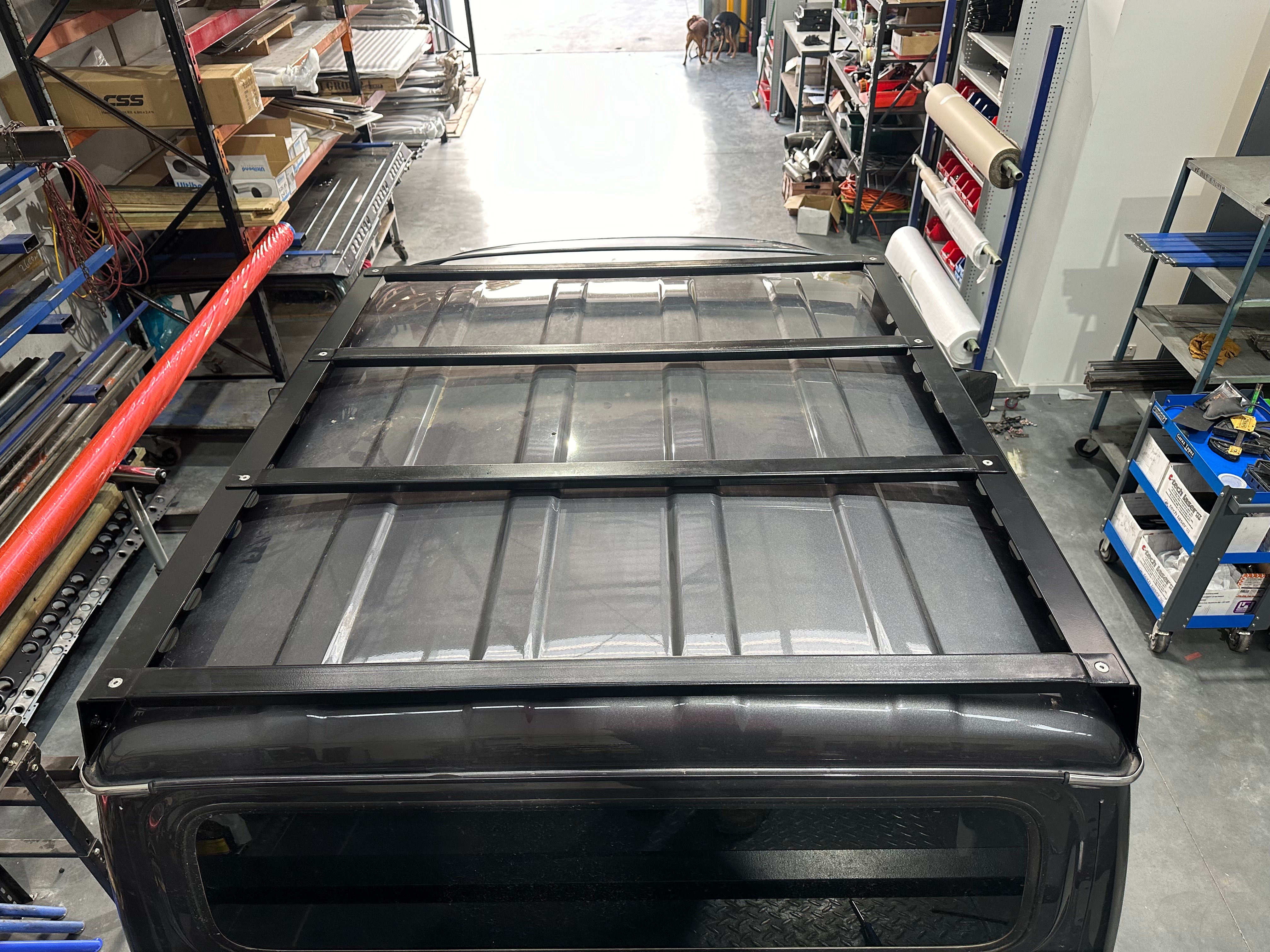 This is an image of a black 4x4 vehicle roof with a Tier One Metalworks custom fabricated roof rack frame installed in a workshop