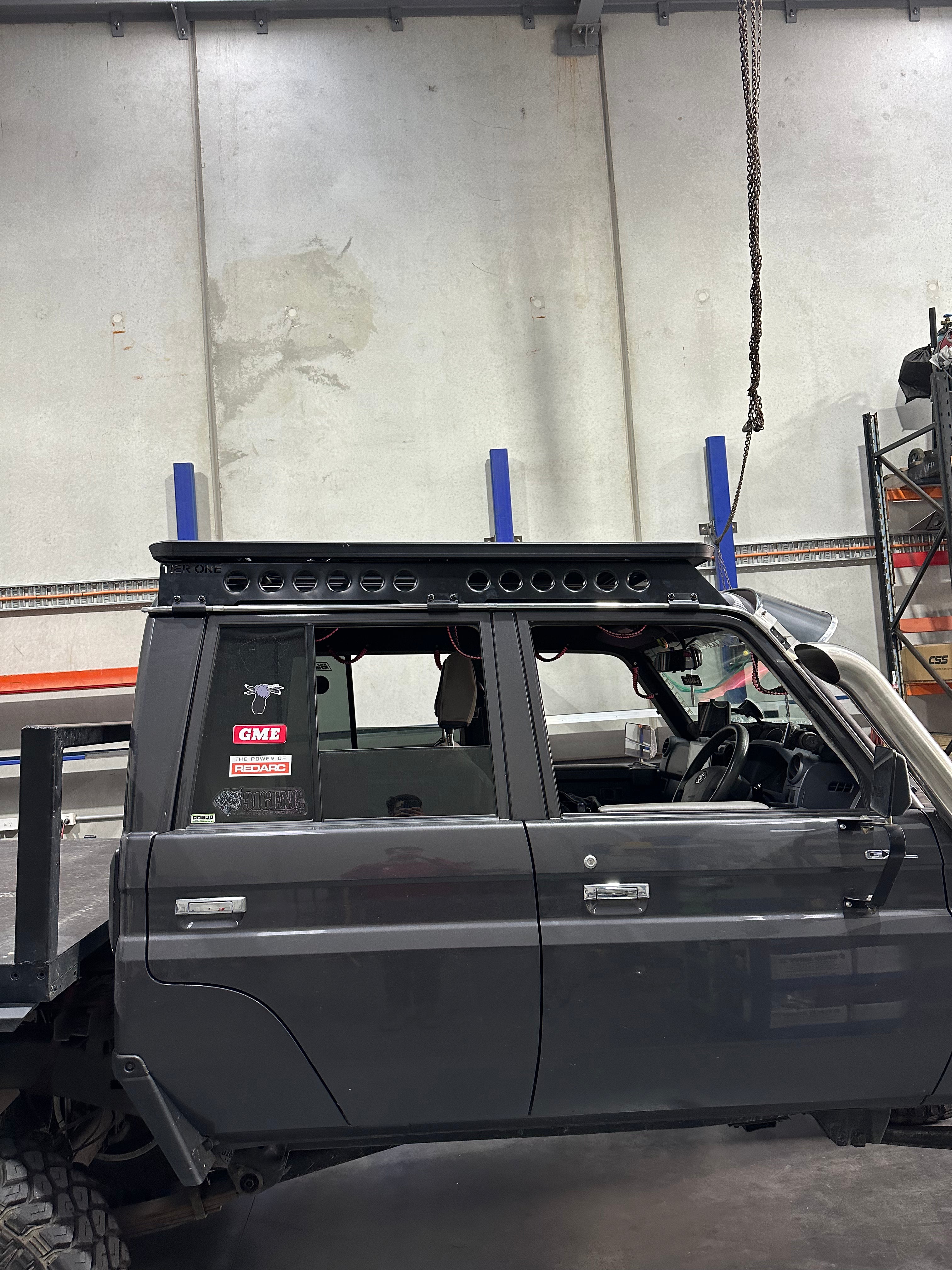 This is an image of a dark grey 4x4 ute with Tier One Metalworks custom roof rack rails installed in a workshop
