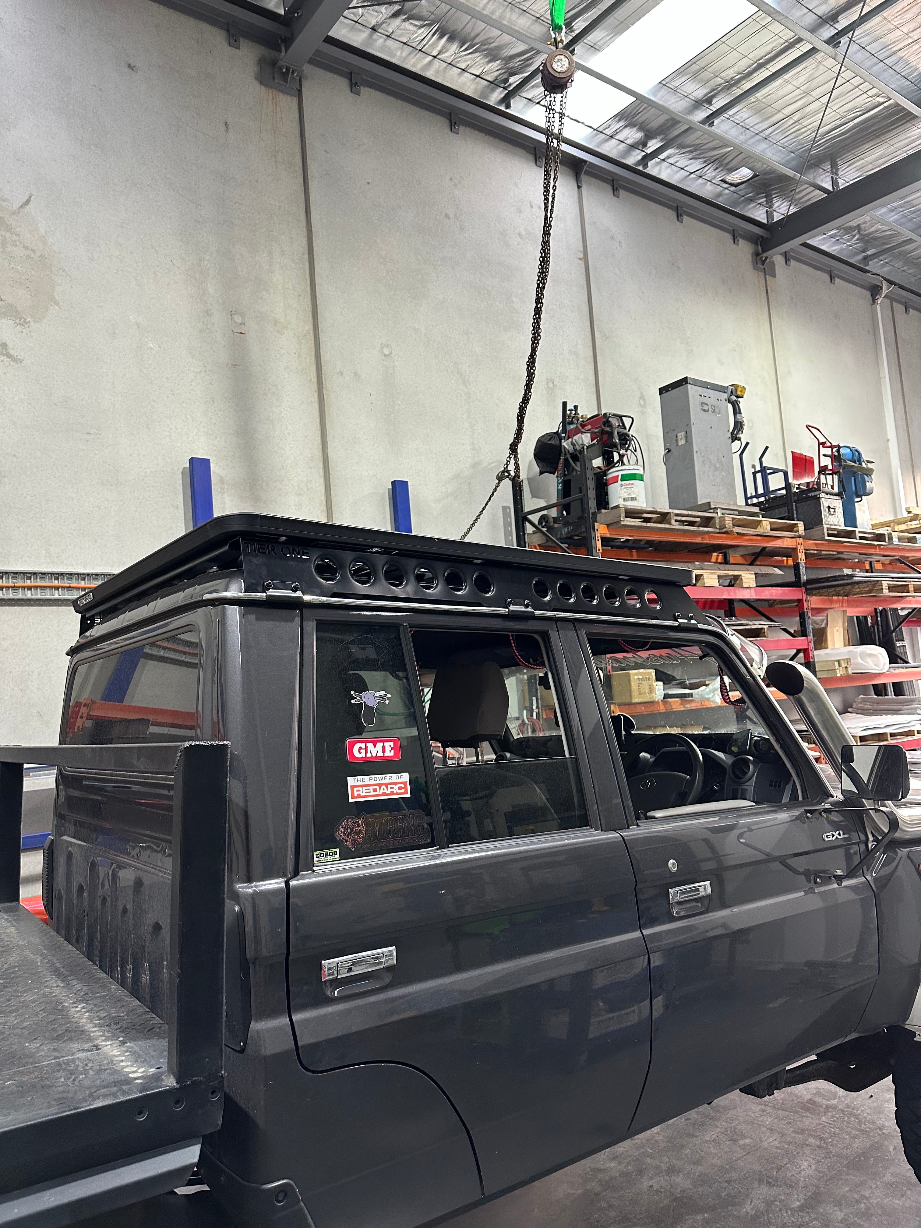 This is an image of a grey 4WD with a custom Tier One Metalworks black roof rack inside a workshop
