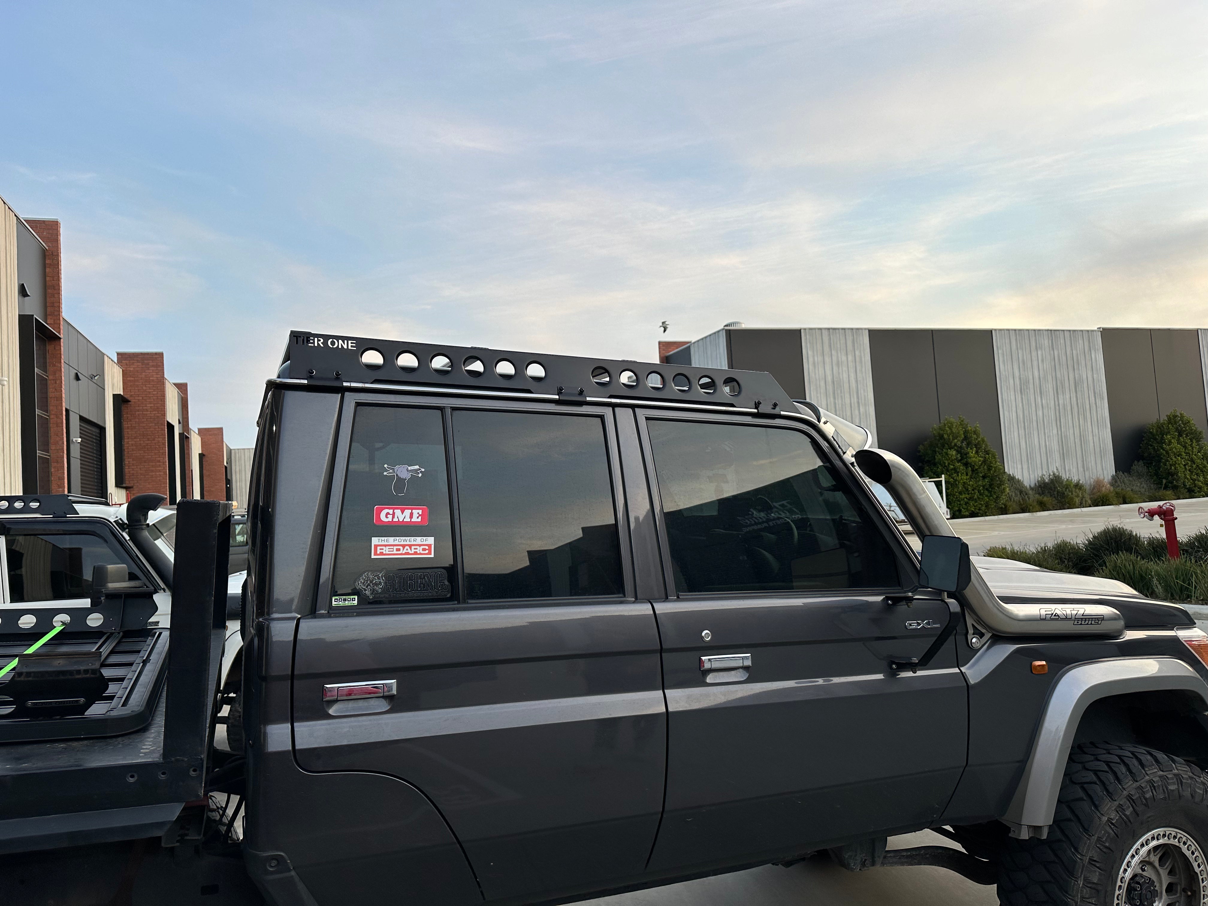This is an image of a grey 4WD fitted with a Tier One Metalworks black roof rack and Fatz Built snorkel in an industrial setting