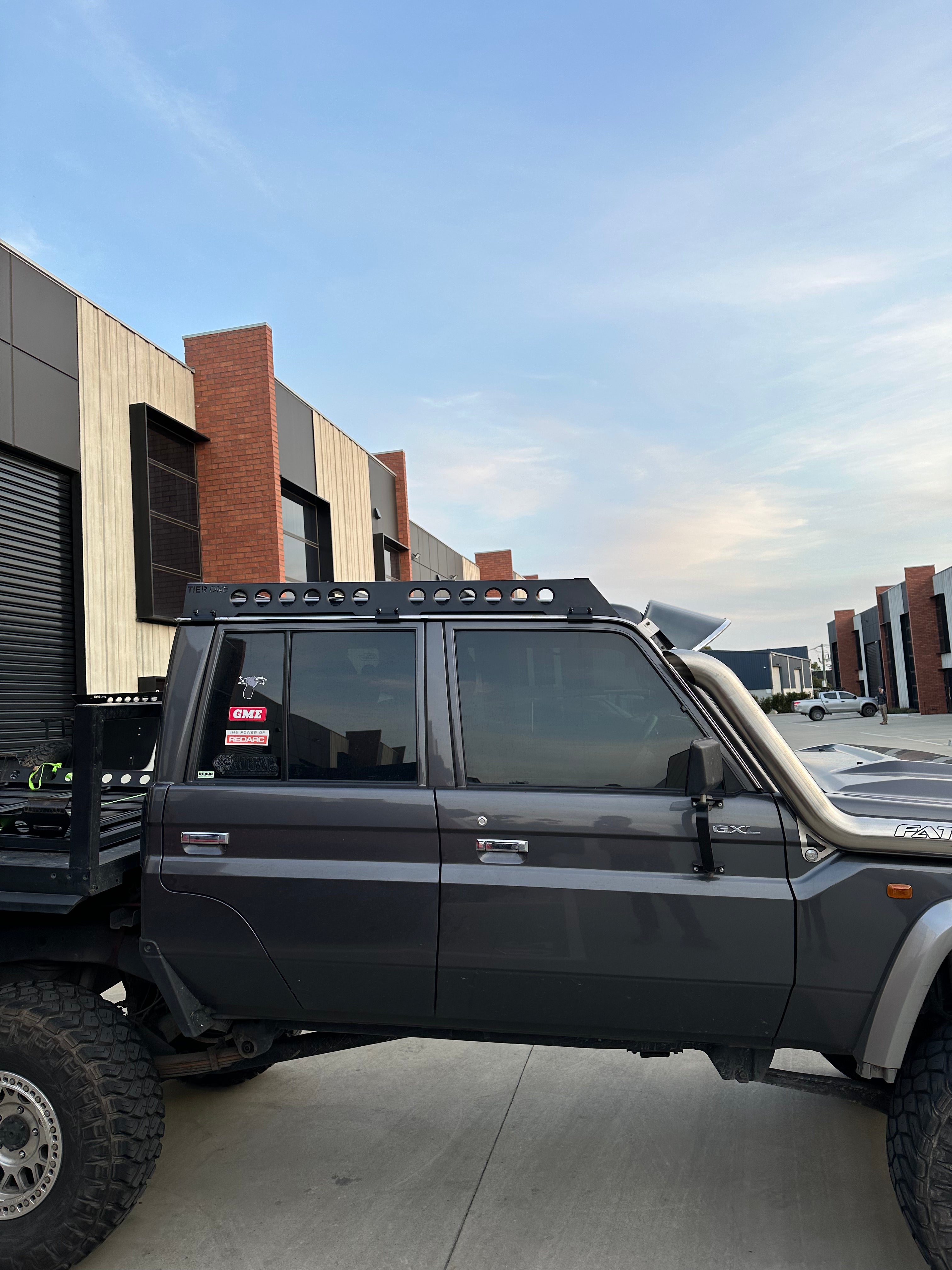 This is an image of a grey Toyota Land Cruiser GXL with Tier One Metalworks roof rack and snorkel in an industrial area