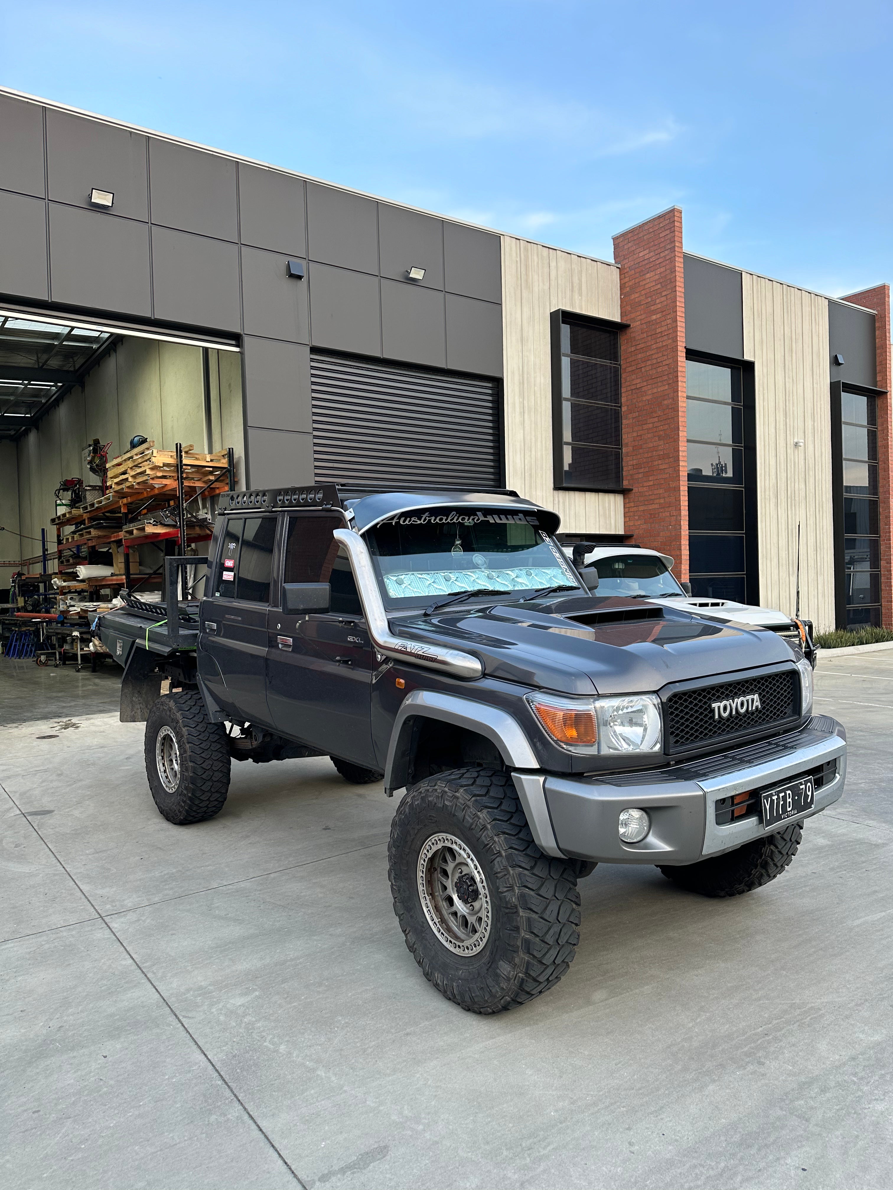 This is an image of a black Toyota 70 Series Land Cruiser with custom 4x4 accessories parked outside an industrial workshop