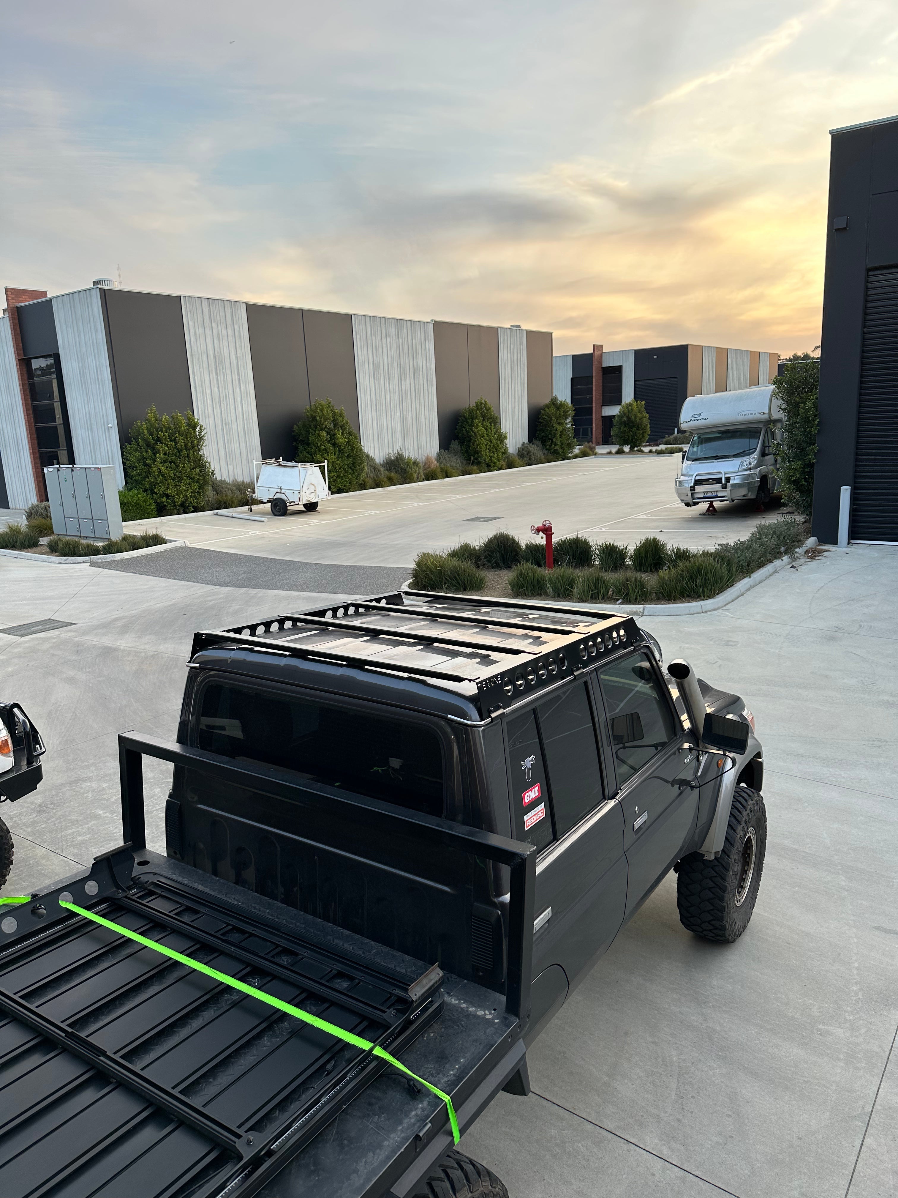 This is an image of a black 4WD ute equipped with Tier One Metalworks roof rack and rails in an industrial area at sunset