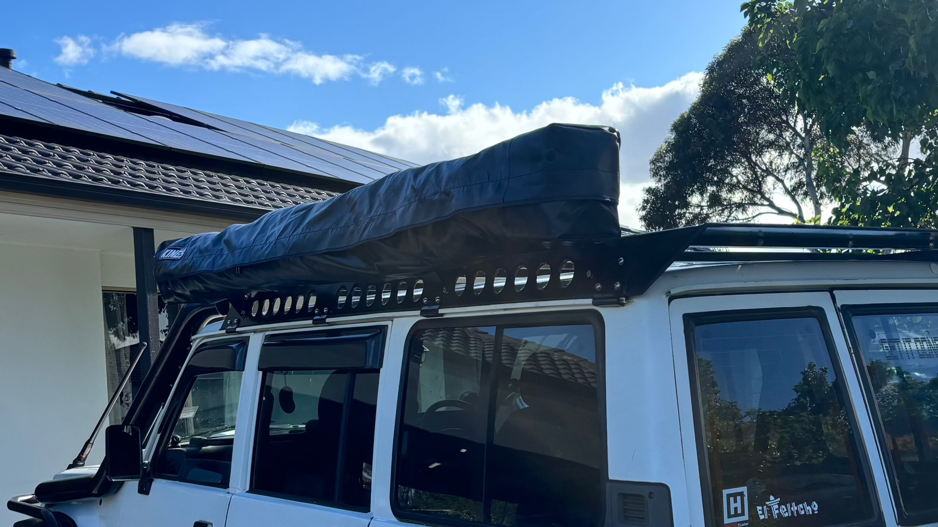 This is an image of a white 4WD with a black roof rack and long black roof top tent cover, fitted by Tier One Metalworks Roof Racks & Rails