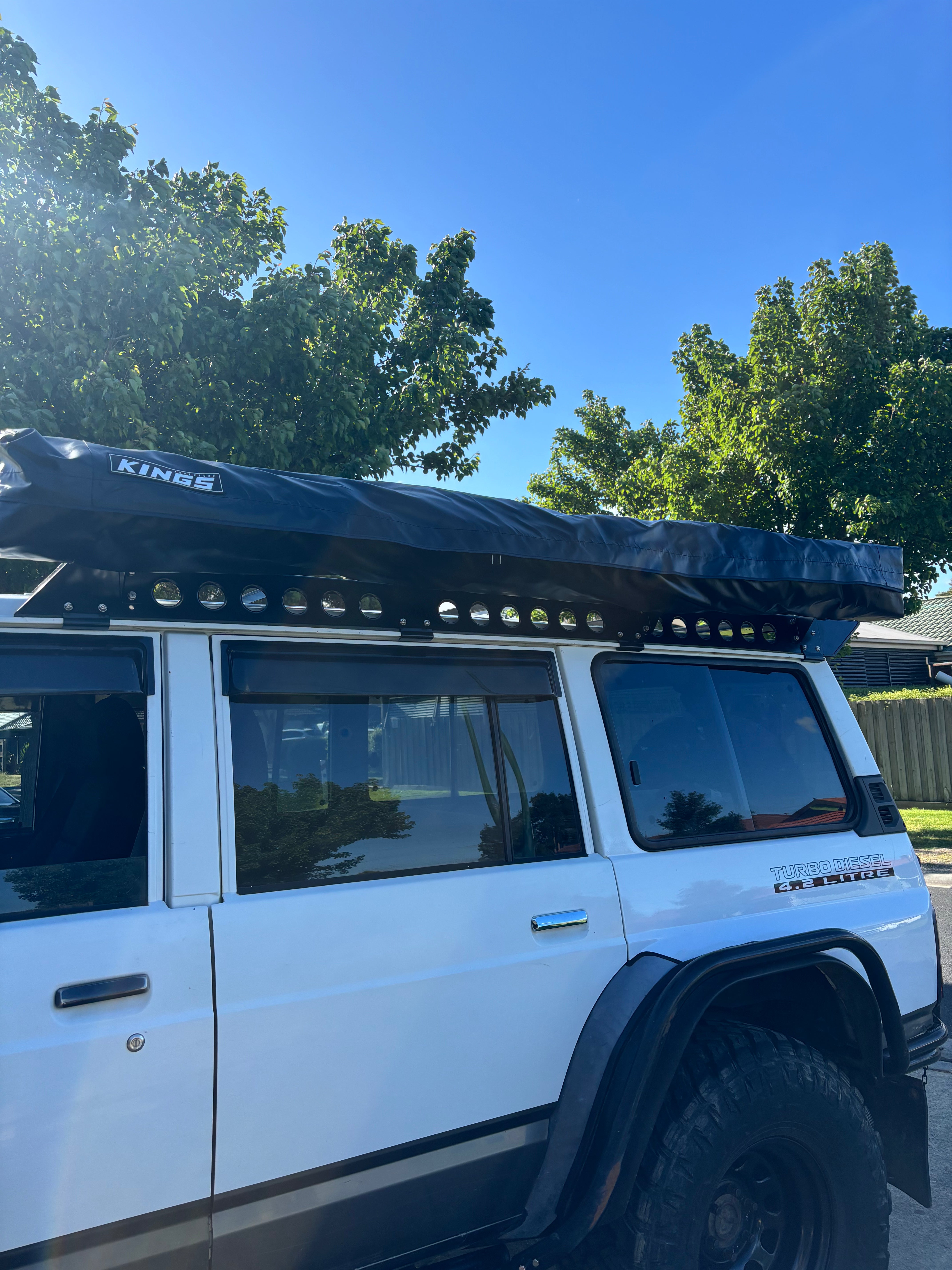 This is an image of a white 4WD with Tier One Metalworks Roof Racks holding a Kings rooftop tent under a clear blue sky