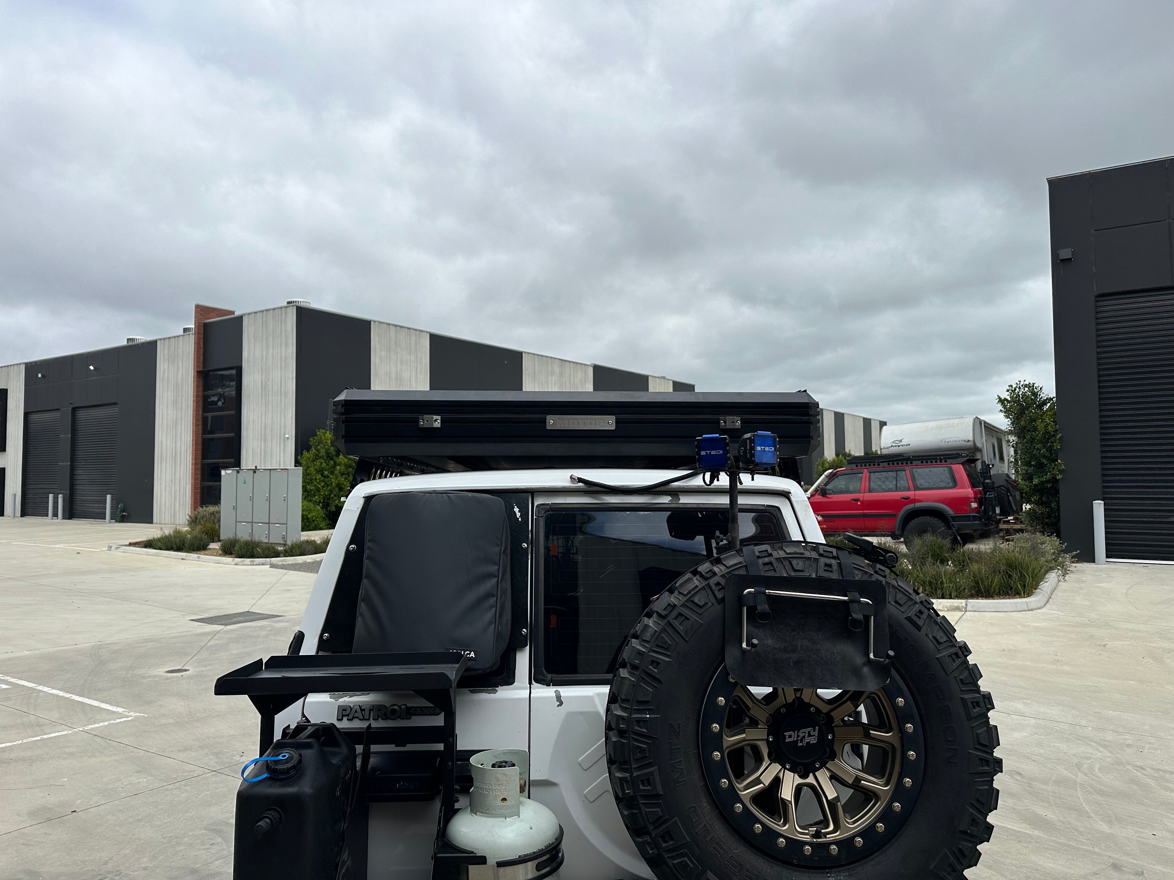 This is an image of a white Nissan Patrol 4x4 with Tier One Metalworks roof rack and rear mounted spare tyre in an industrial area