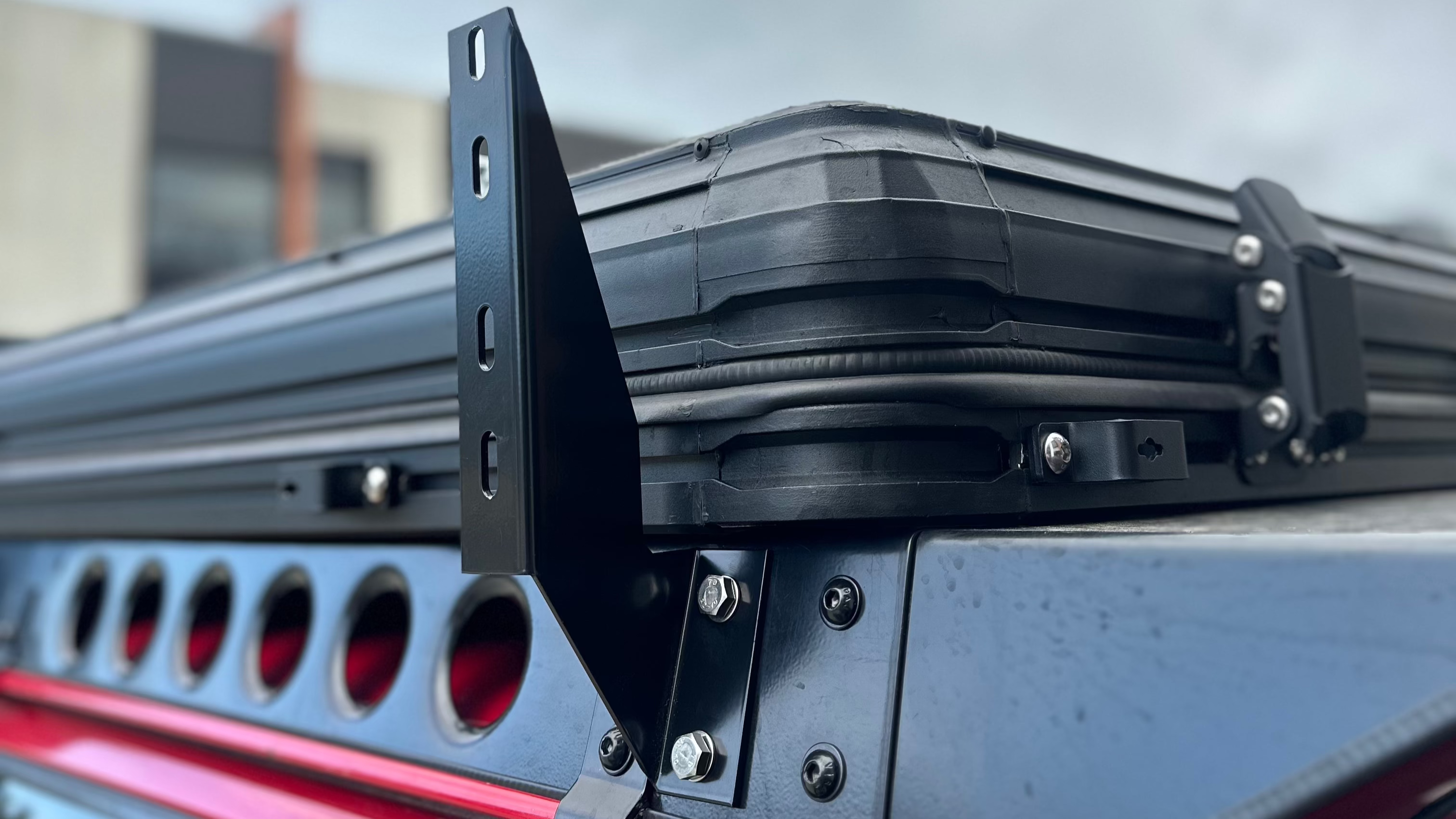 This is an image of a black rooftop tent mounted on a black Tier One Metalworks roof rack on a red 4WD vehicle