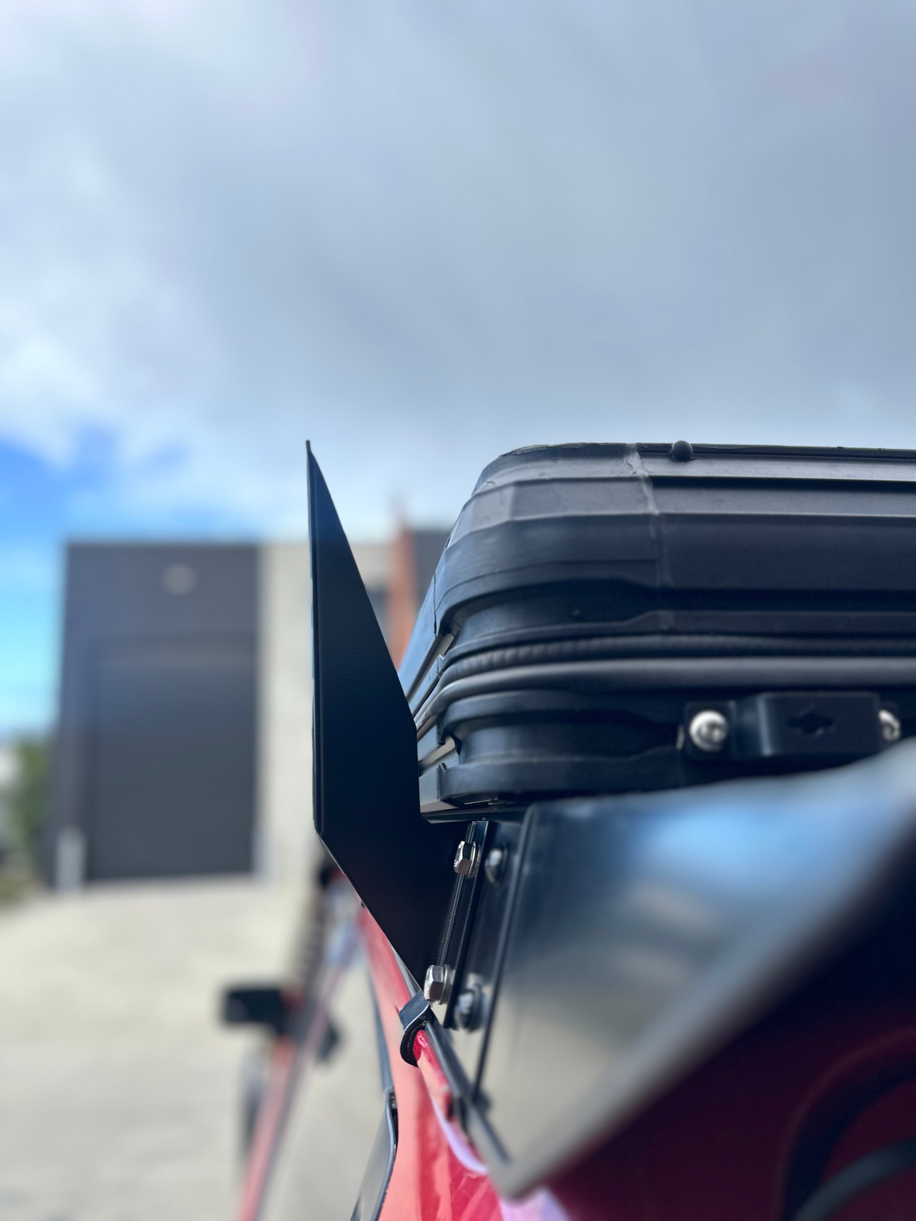 This is an image of a black metal roof rack mounted on a red vehicle, showcasing Tier One Metalworks roof racks and rails