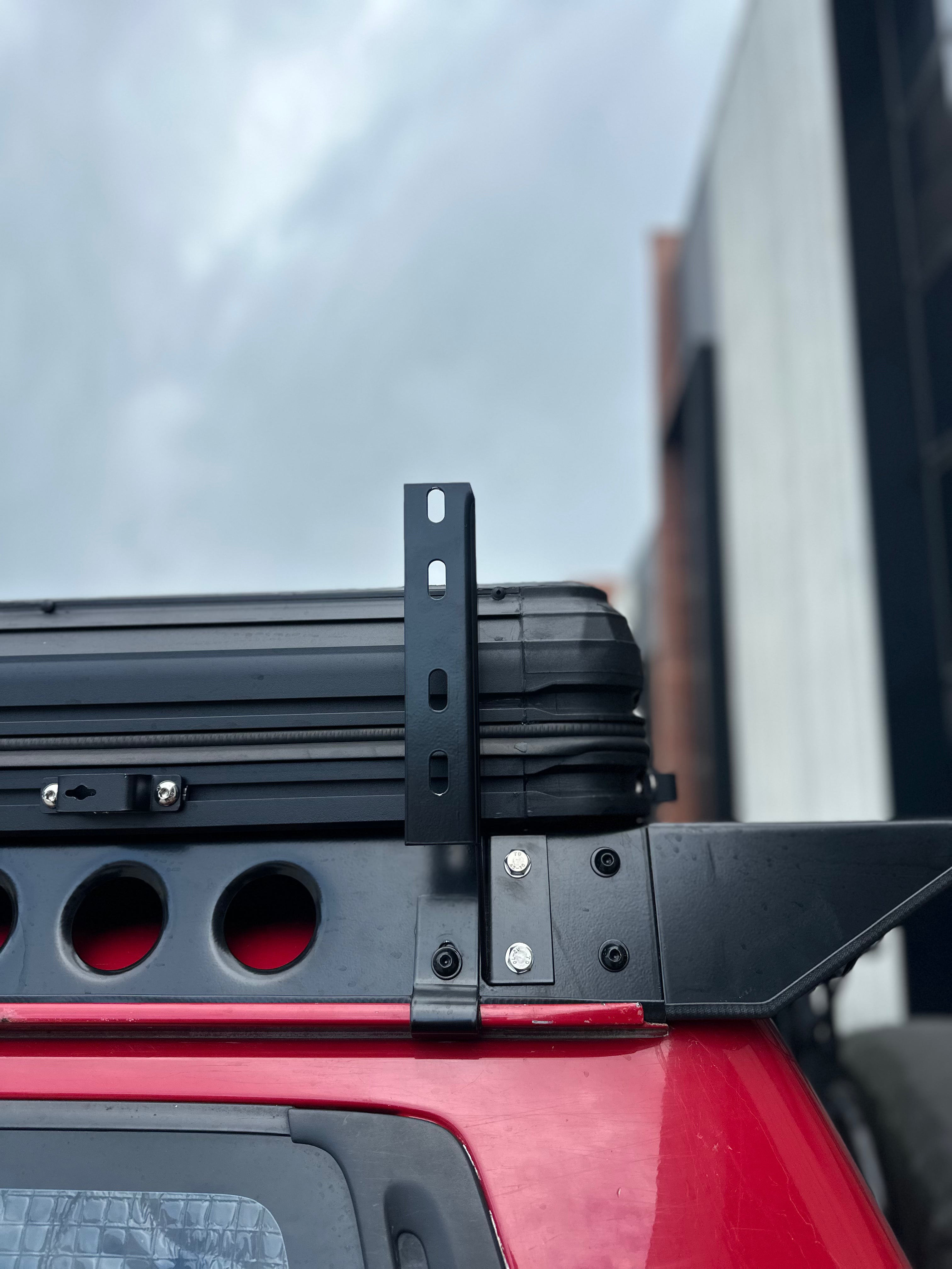 This is an image of a black Tier One Metalworks roof rack mounted on a red 4x4 vehicle, showing metal brackets and a rooftop storage box