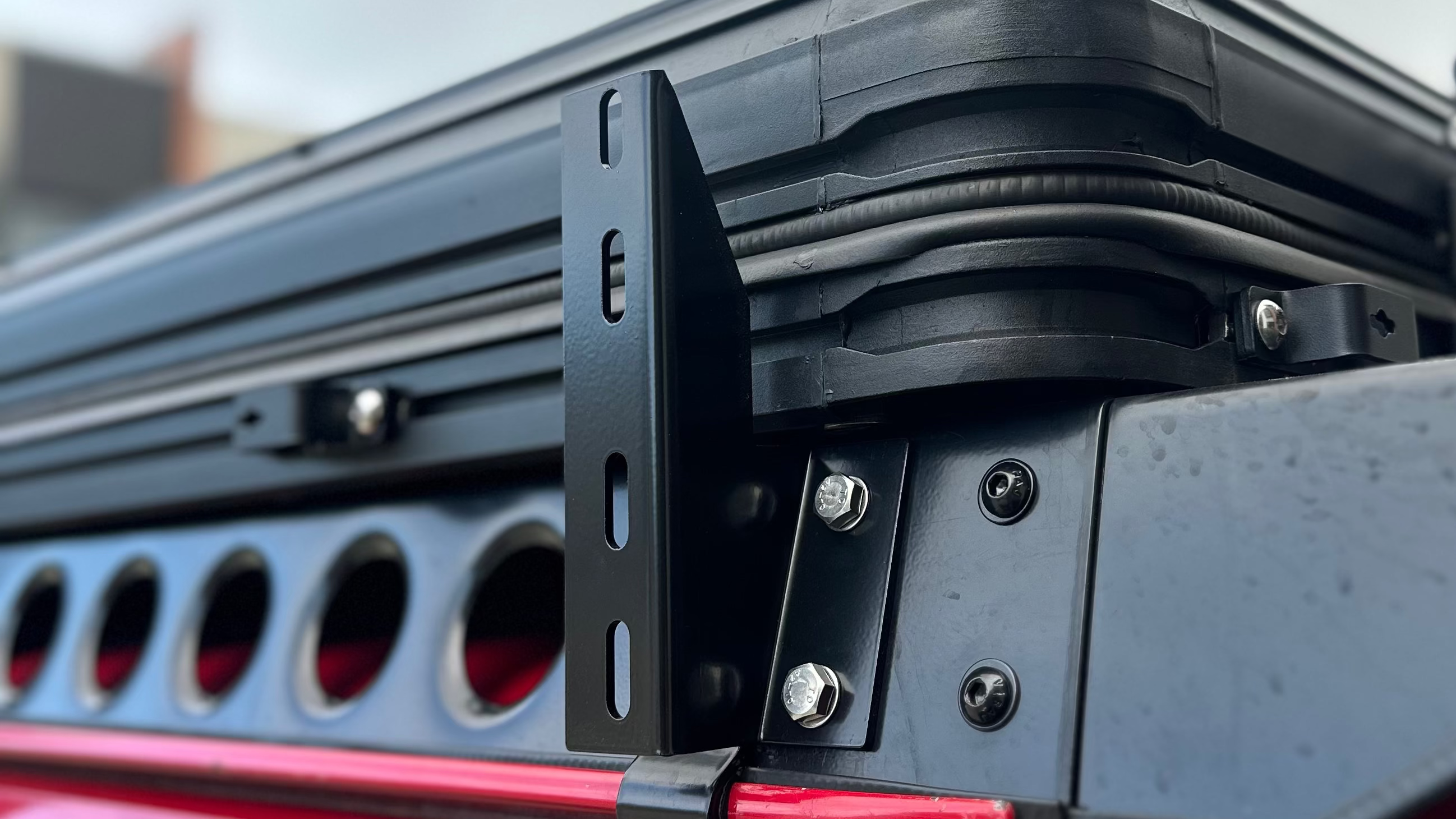 This is an image of a black metal bracket and mounting bolts on a red 4x4 vehicle, part of Tier One Metalworks roof rack system