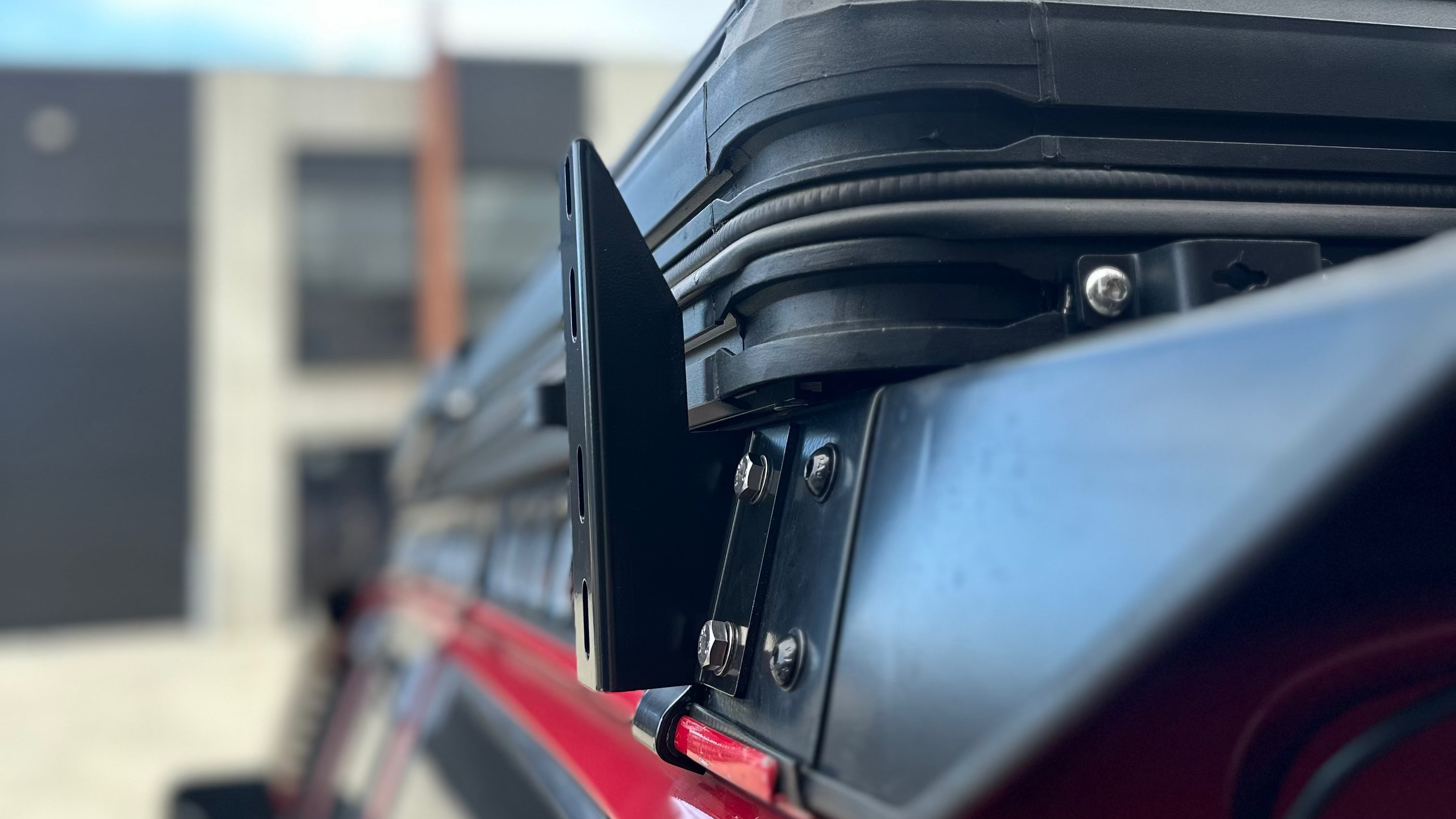 This is an image of a black rooftop tent mounted on a Tier One Metalworks roof rack on a red 4WD vehicle
