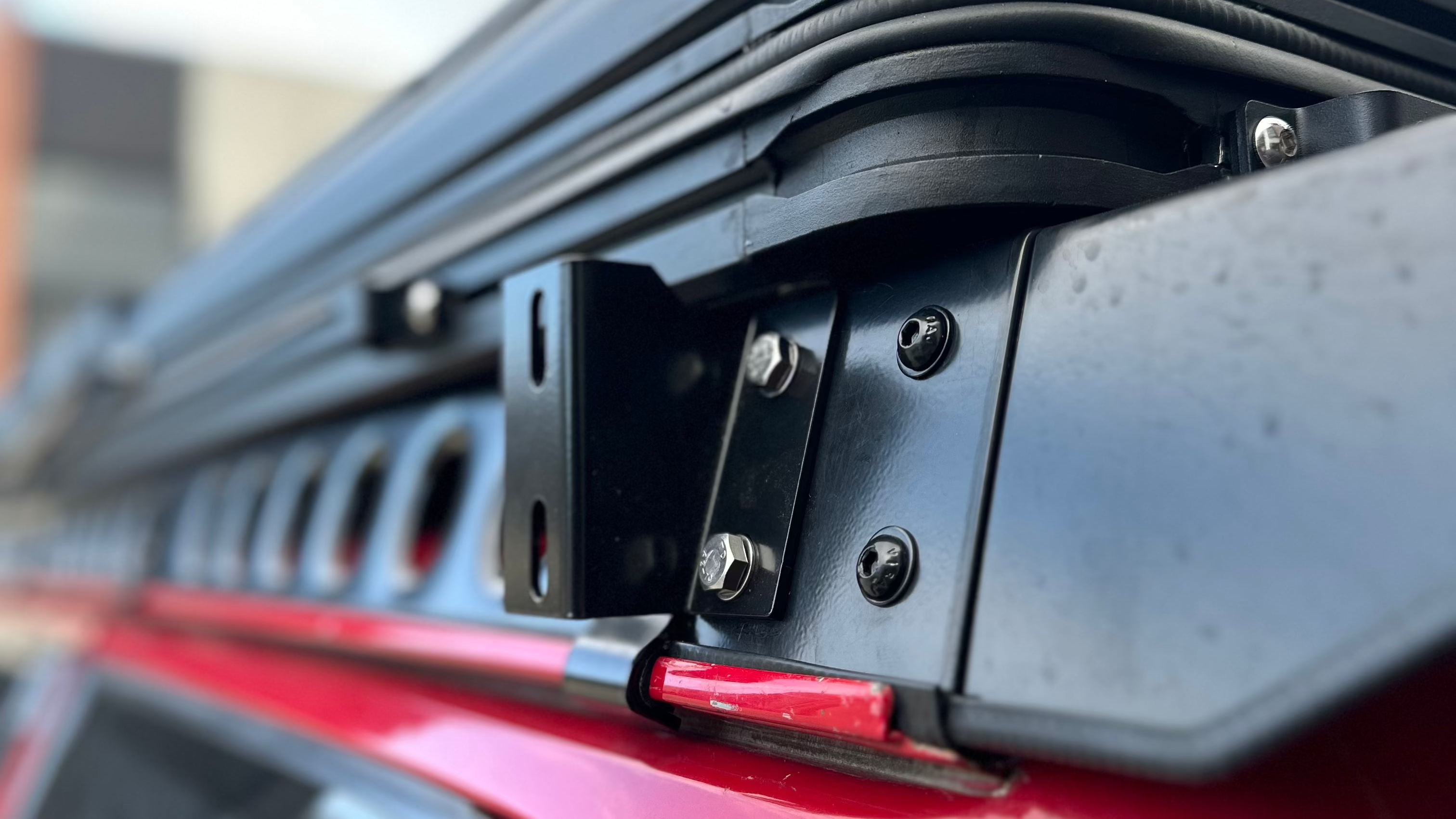 This is an image of a black metal roof rack mount bolt and bracket on a red 4WD vehicle, Tier One Metalworks Roof Racks & Rails