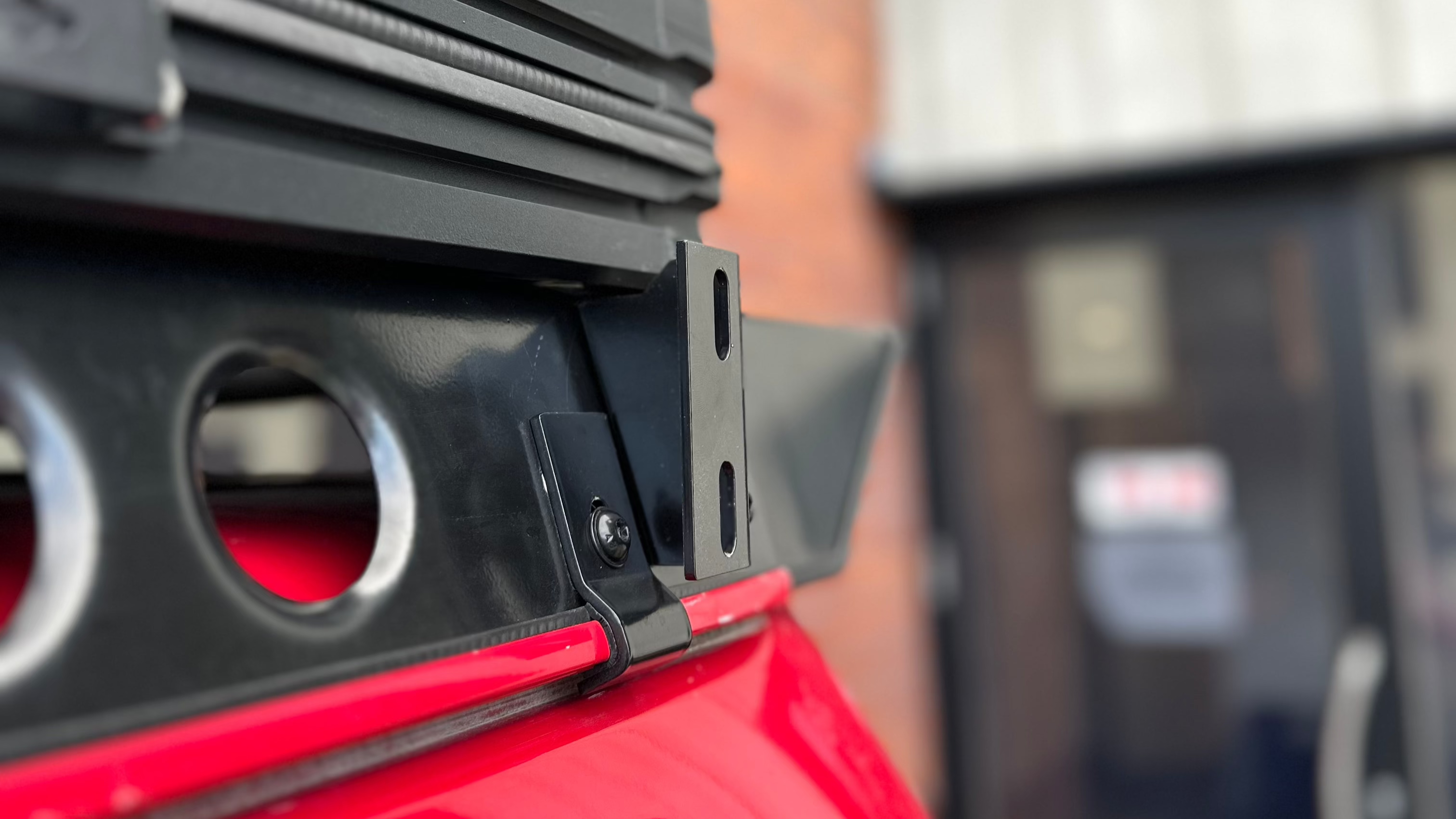 This is an image of a close-up black metal bracket mounted on a red vehicle panel, likely part of a Tier One Metalworks roof rack or rail system.
