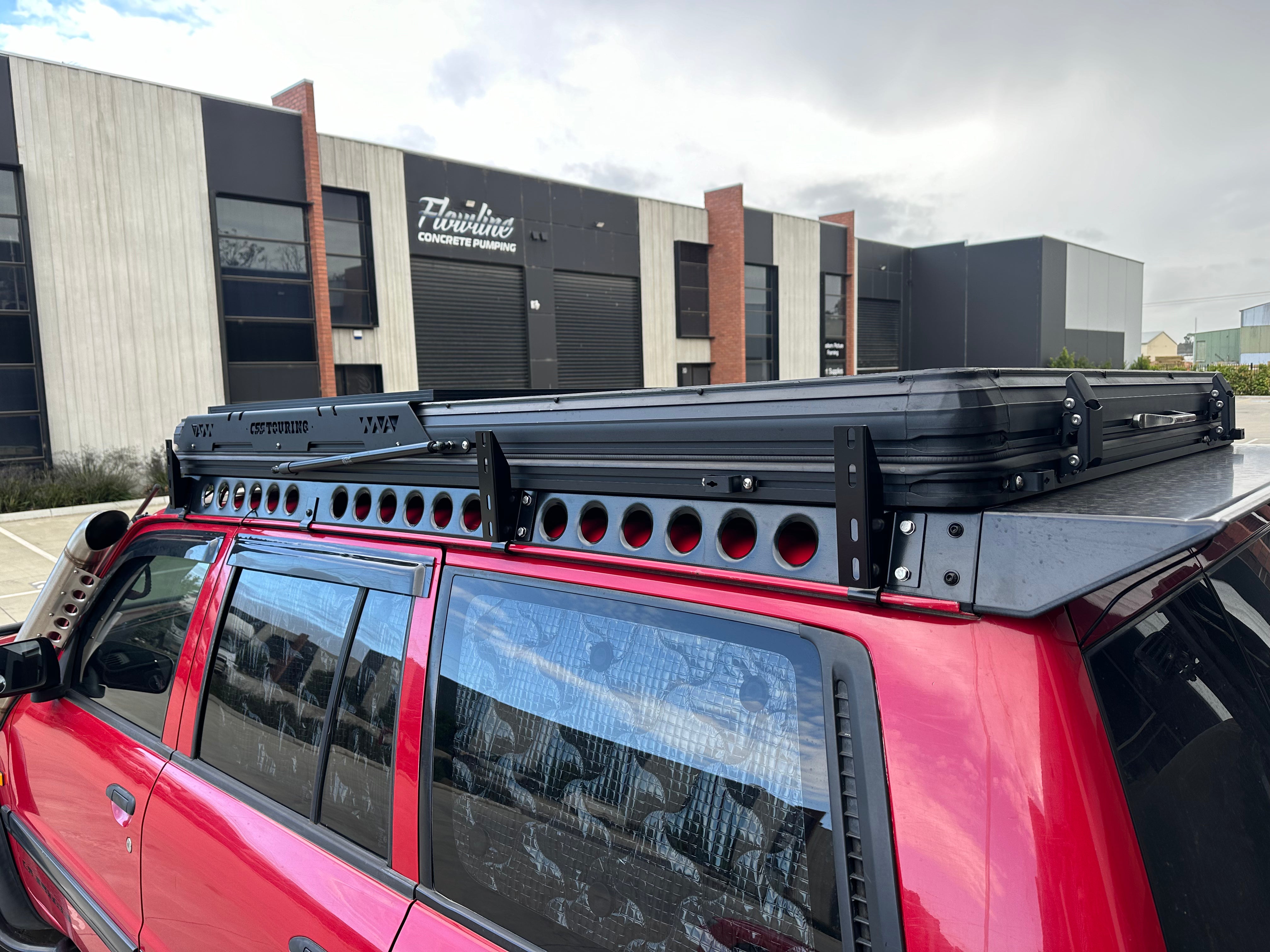 This is an image of a red 4WD with a custom black Tier One Metalworks roof rack and CSS Touring rooftop tent installed on the roof.