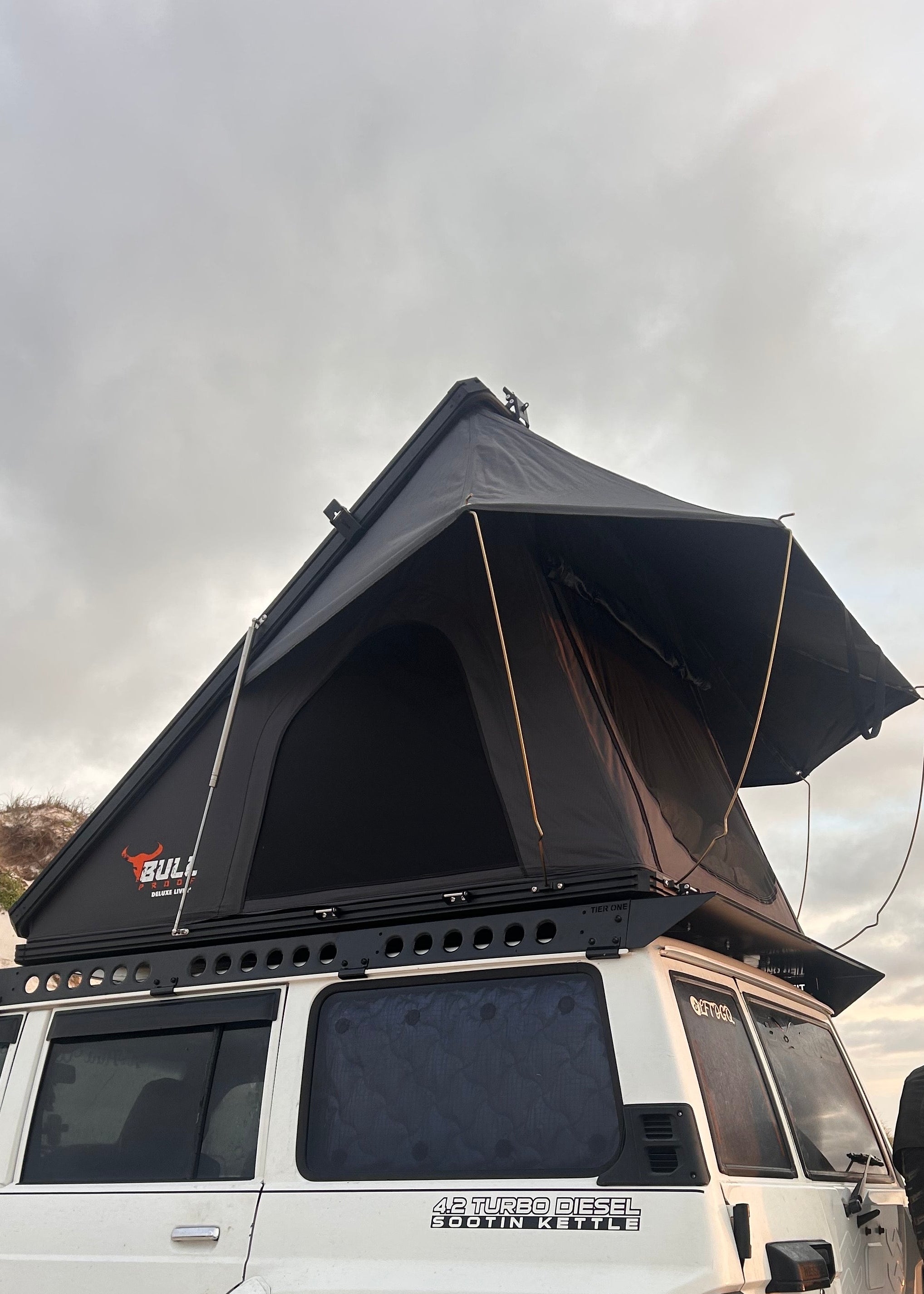 This is an image of a white 4.2 Turbo Diesel 4WD with a black Tier One Metalworks roof rack and Bull 4x4 rooftop tent