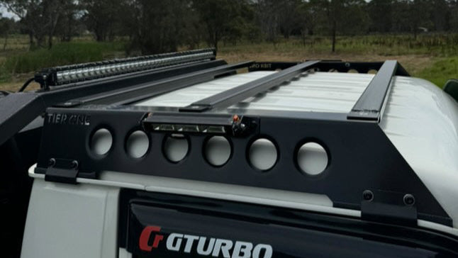 This is an image of a white 4x4 with a black Tier One Metalworks roof rack and light bar, showcasing custom 4WD accessories