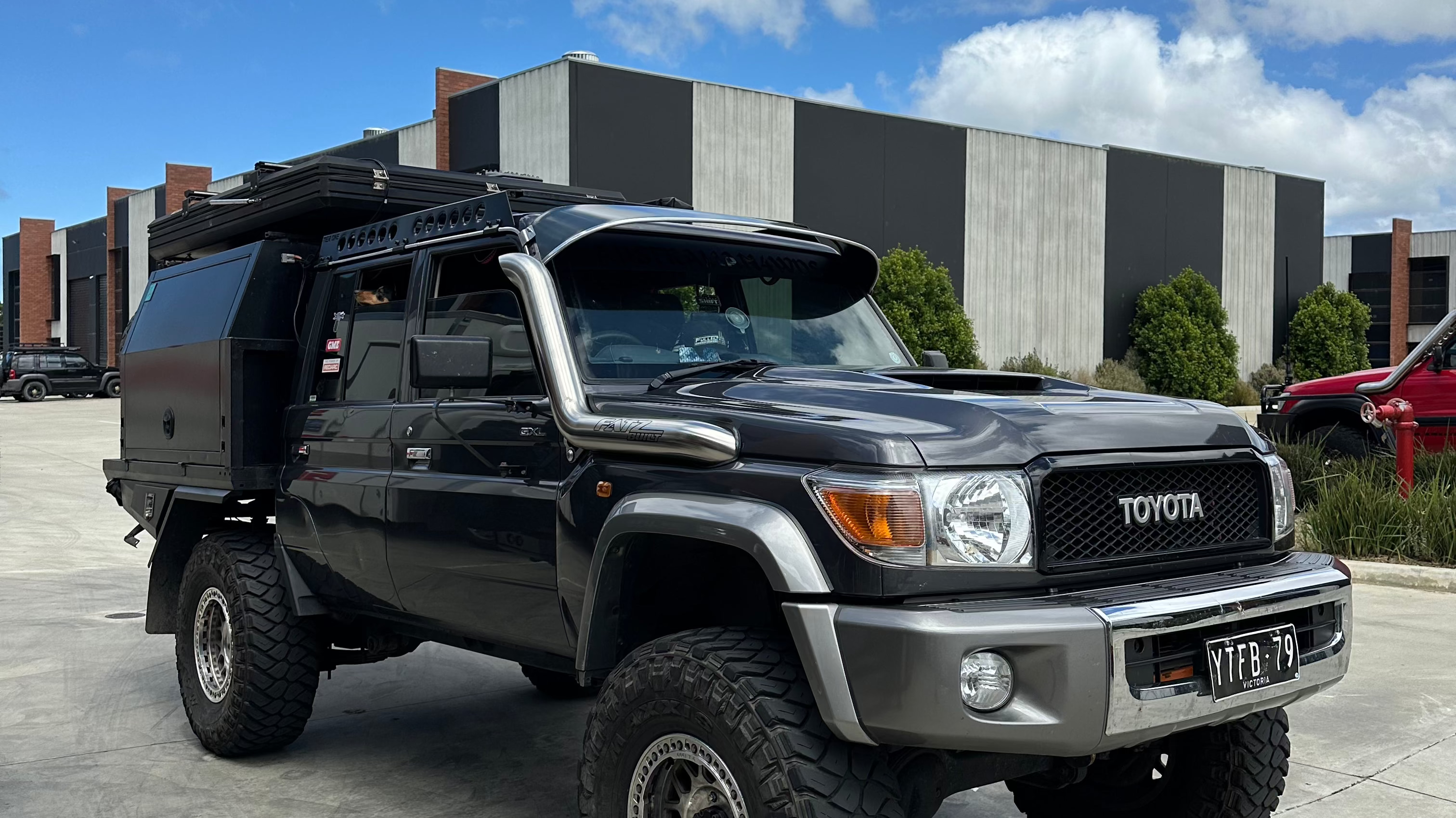 This is an image of a black Toyota Land Cruiser 79 Series with Tier One Metalworks roof rack and rear tray, parked in an industrial area