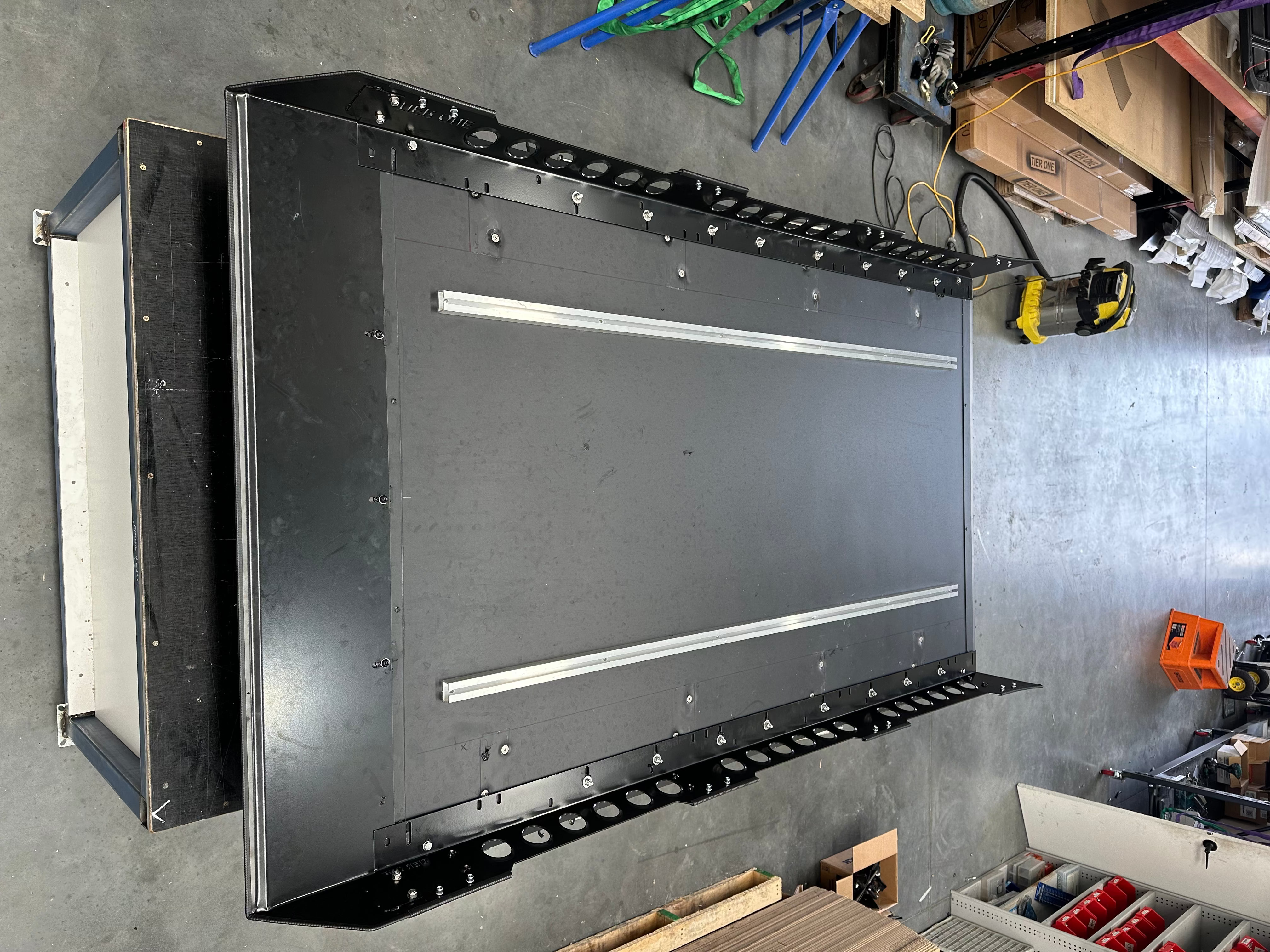 This is an image of a black metal 4x4 roof rack tray with side rails from Tier One Metalworks in an industrial workshop.