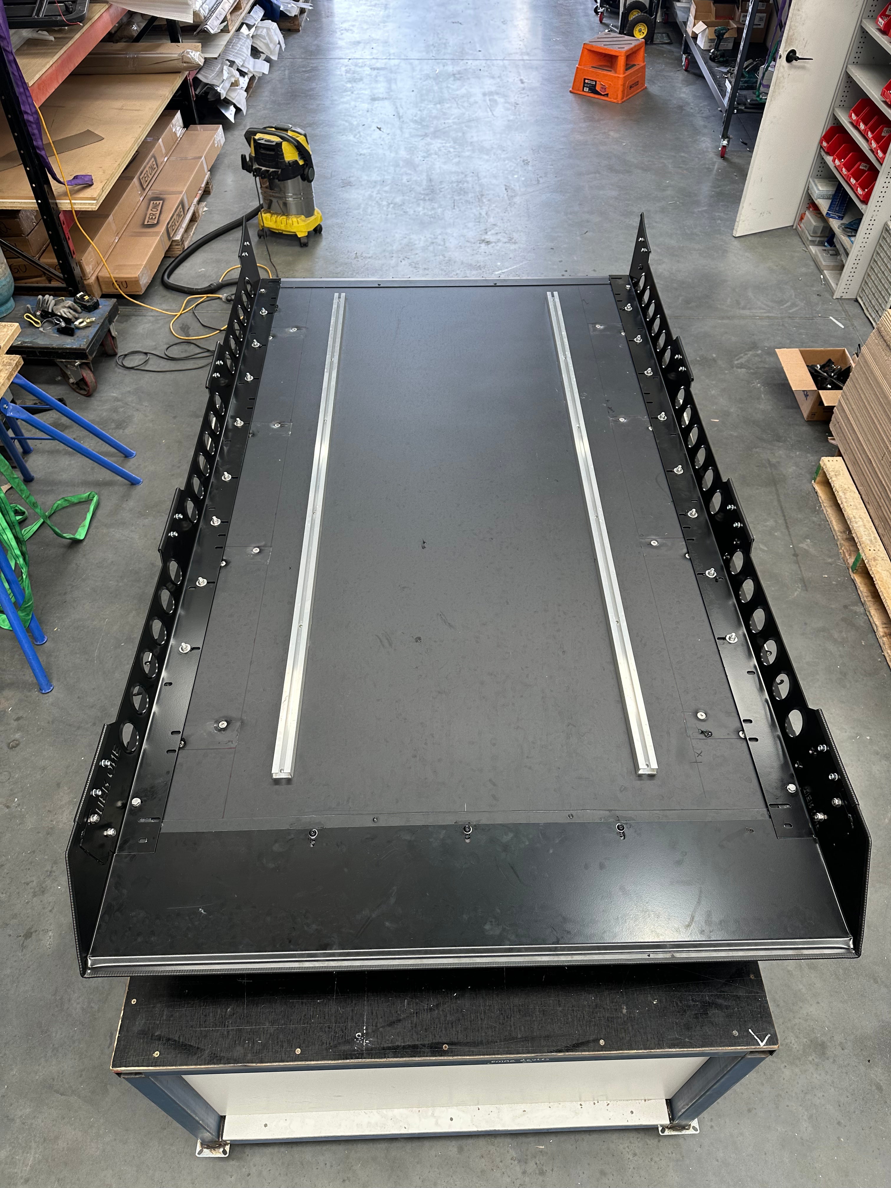 This is an image of a black Tier One Metalworks 4WD roof rack platform with side rails in a workshop setting