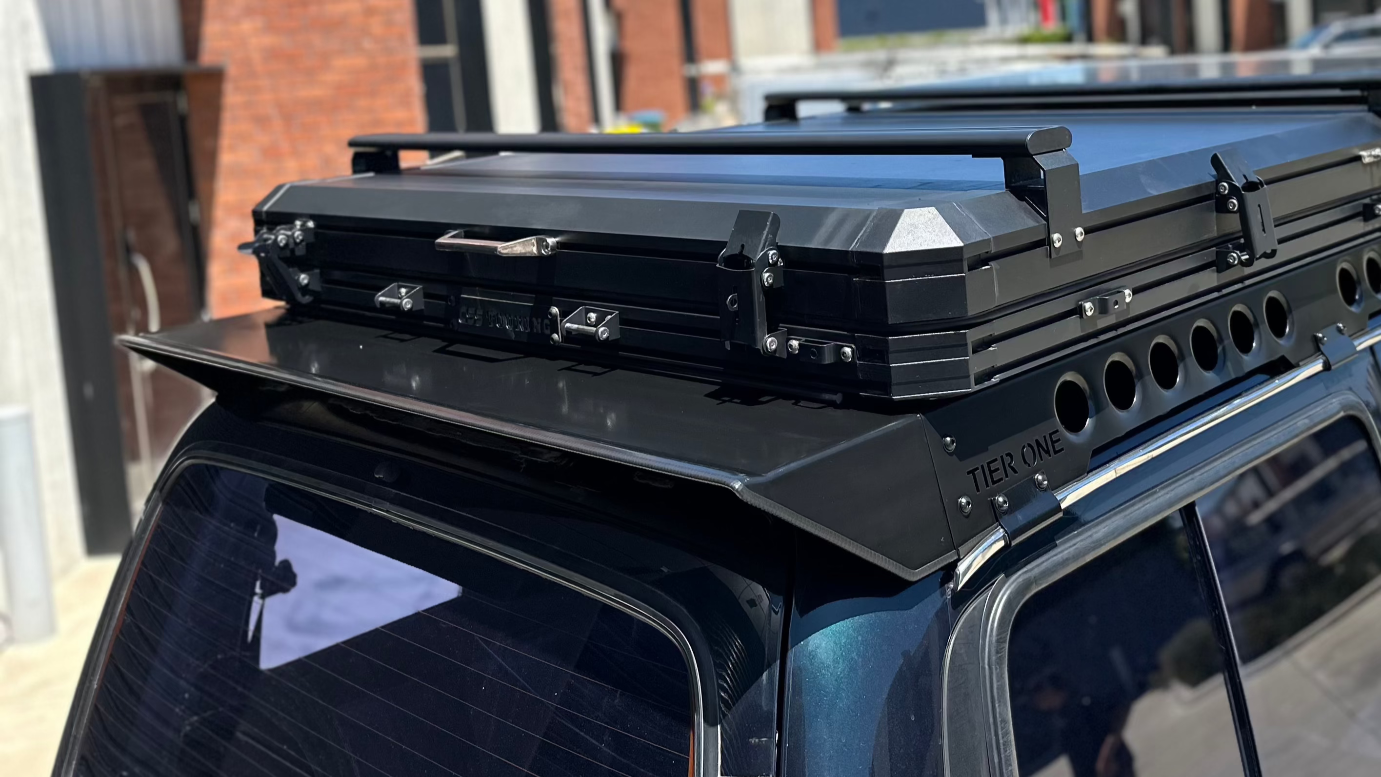 This is an image of a black folded rooftop tent mounted on blue 4x4 with Tier One Metalworks roof racks and rails