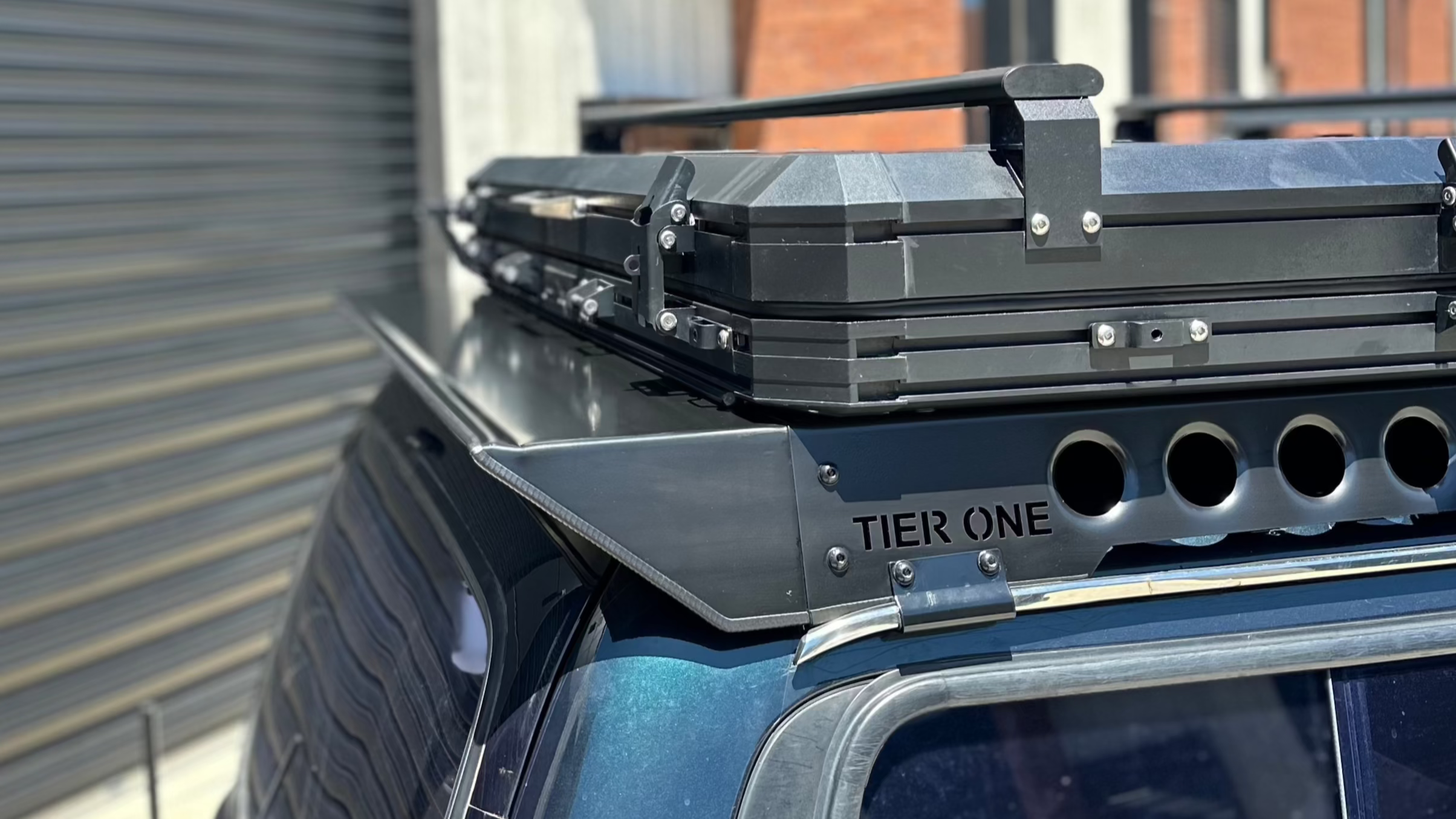 This is an image of a blue 4x4 with a Tier One Metalworks black roof rack and mounted rooftop tent