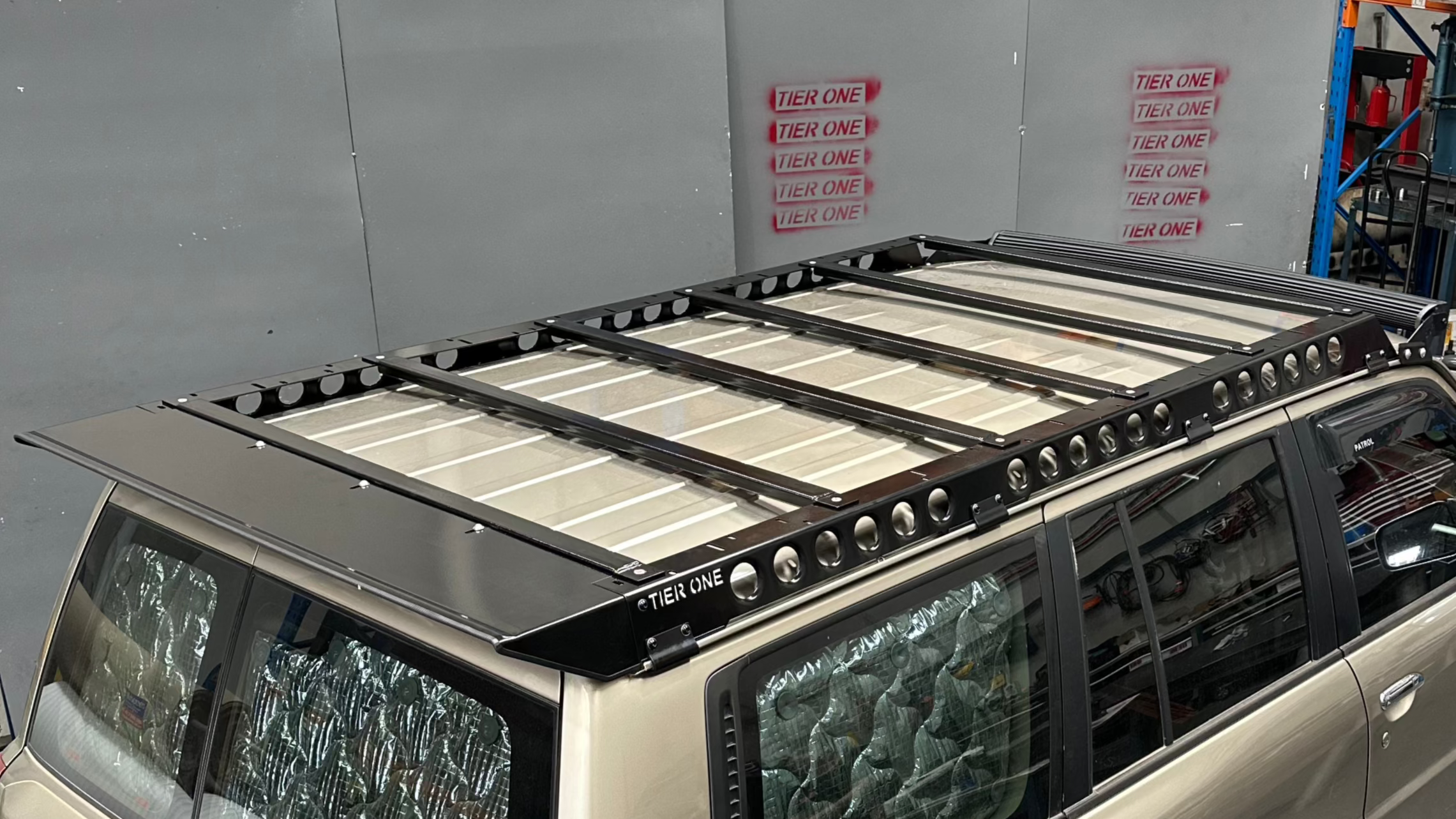 This is an image of a silver Nissan Patrol fitted with a Tier One Metalworks black steel roof rack and rails