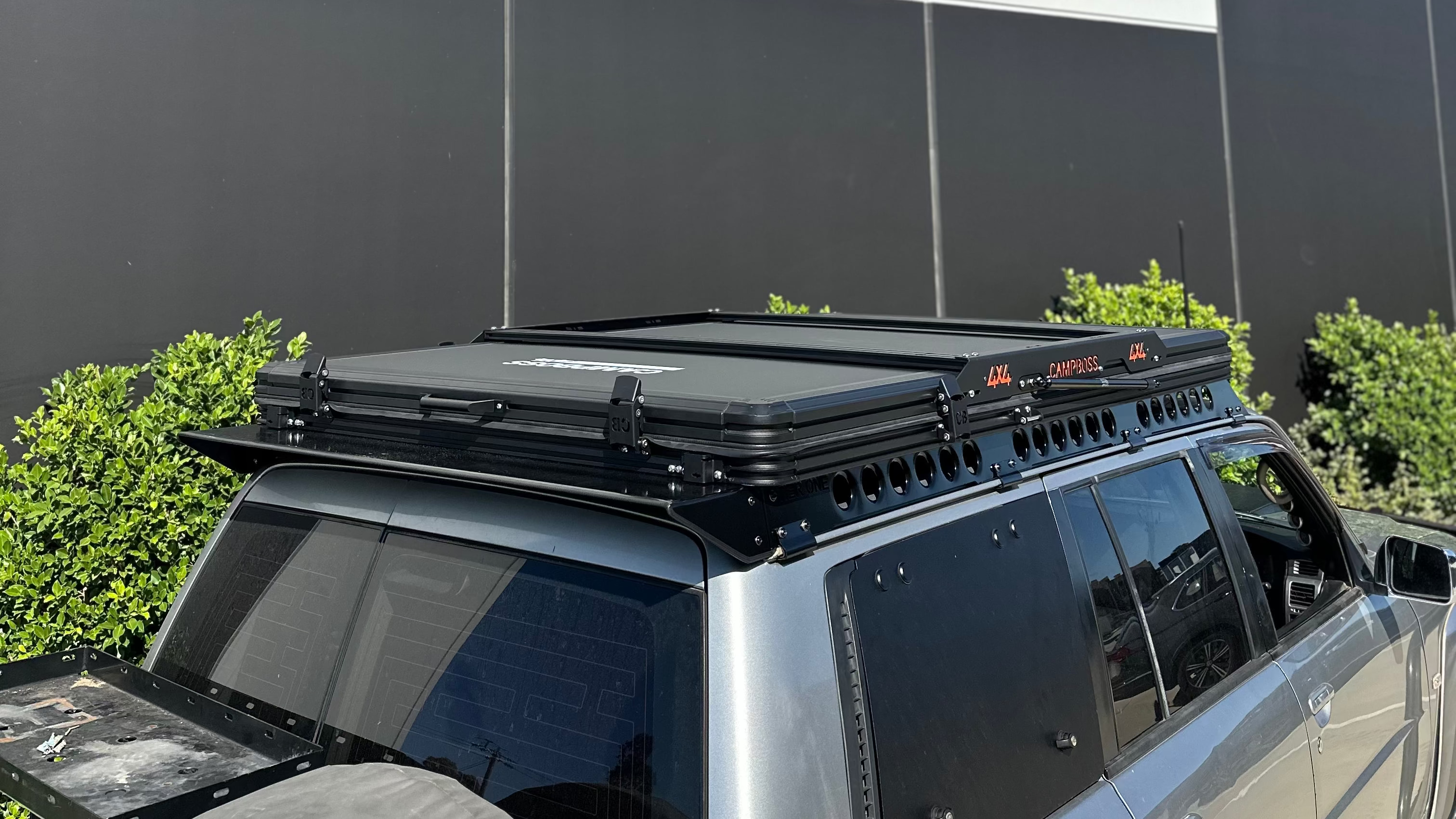 This is an image of a silver 4x4 fitted with a black Tier One Metalworks Roof Rack & Rails and a Campboss rooftop tent on a sunny day
