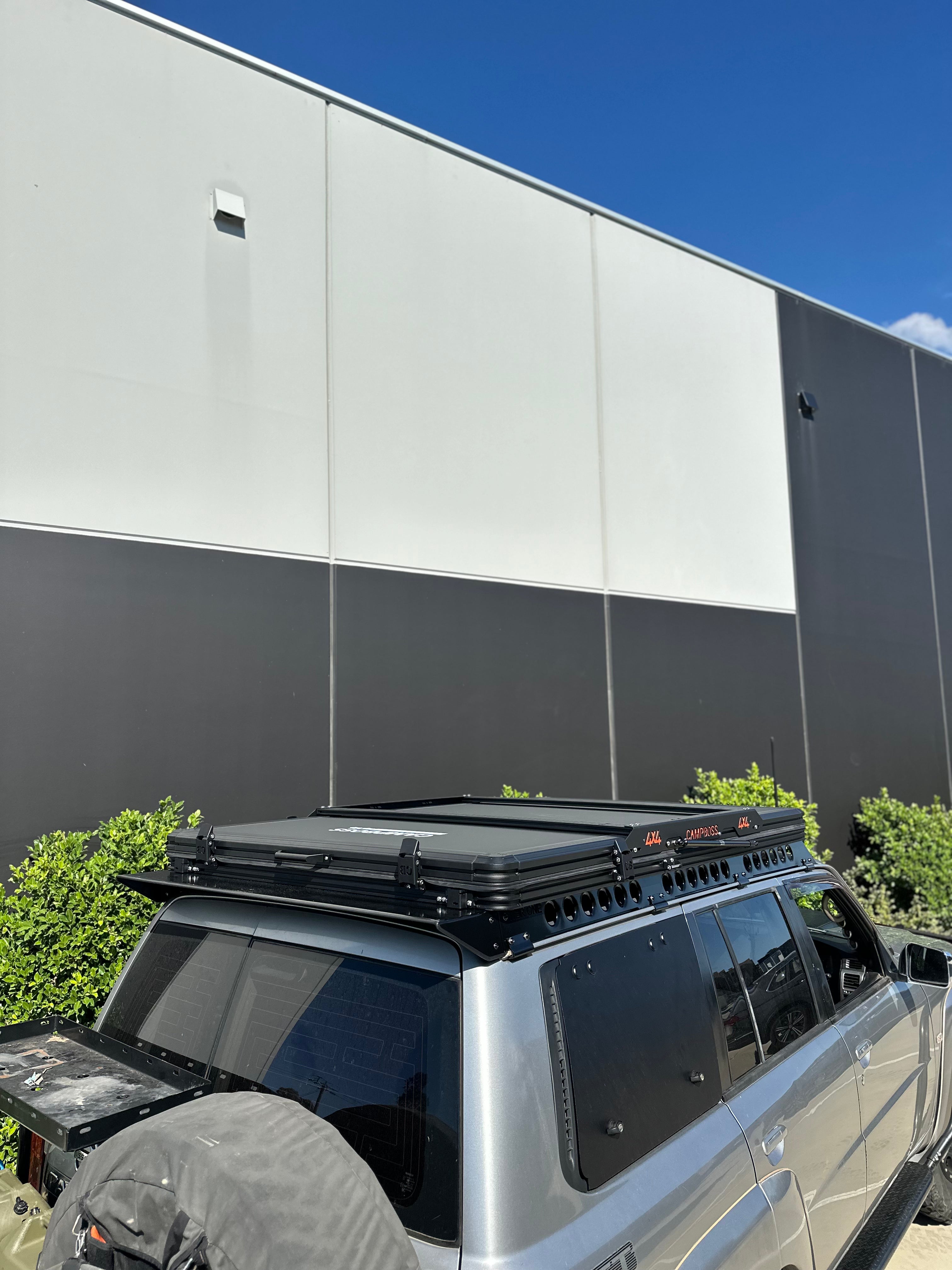 This is an image of a silver 4x4 fitted with a black Tier One Metalworks Roof Rack & Rails and a Campboss rooftop tent on a sunny day