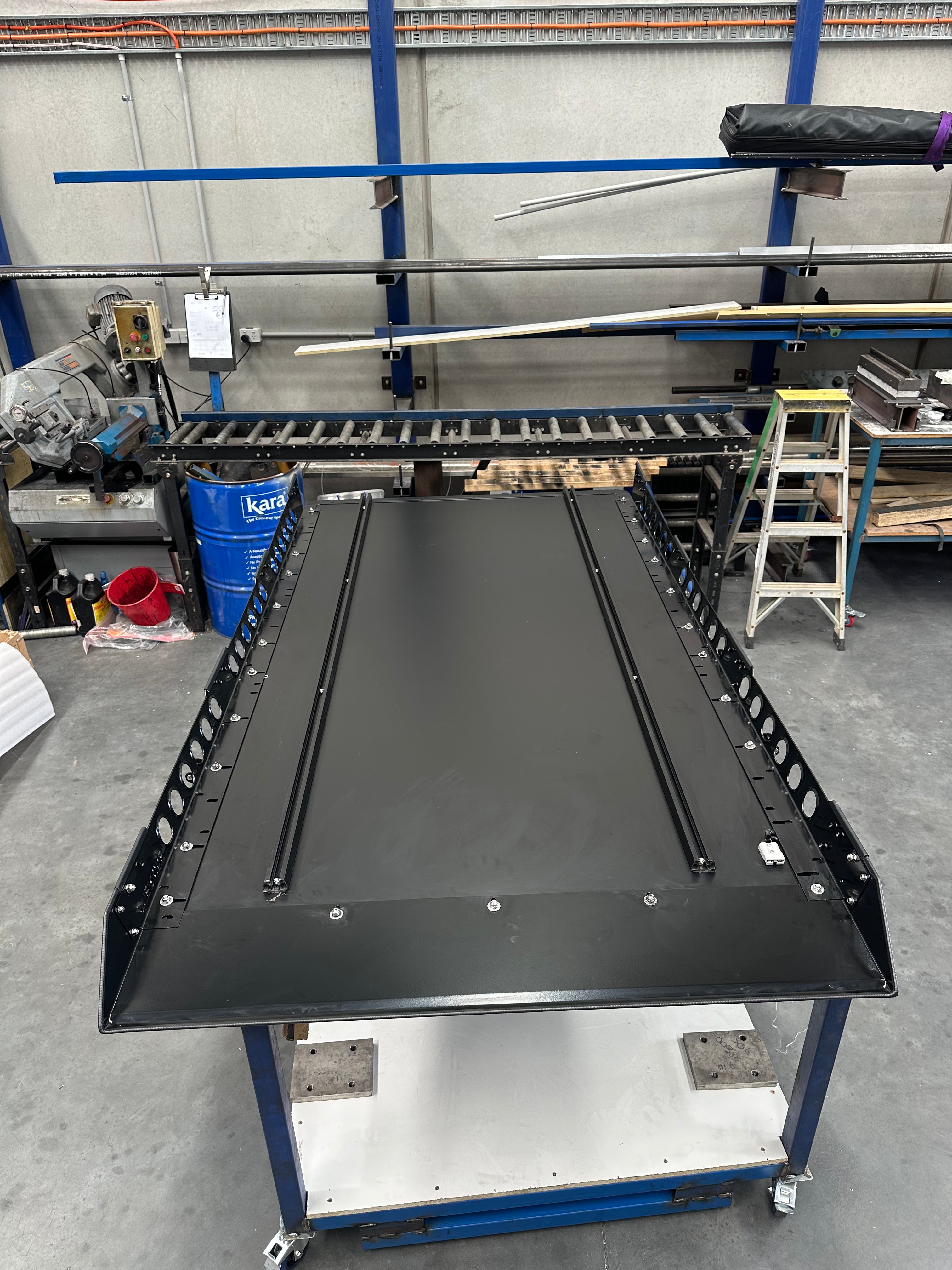 This is an image of a black metal roof rack tray by Tier One Metalworks in an industrial workshop setting
