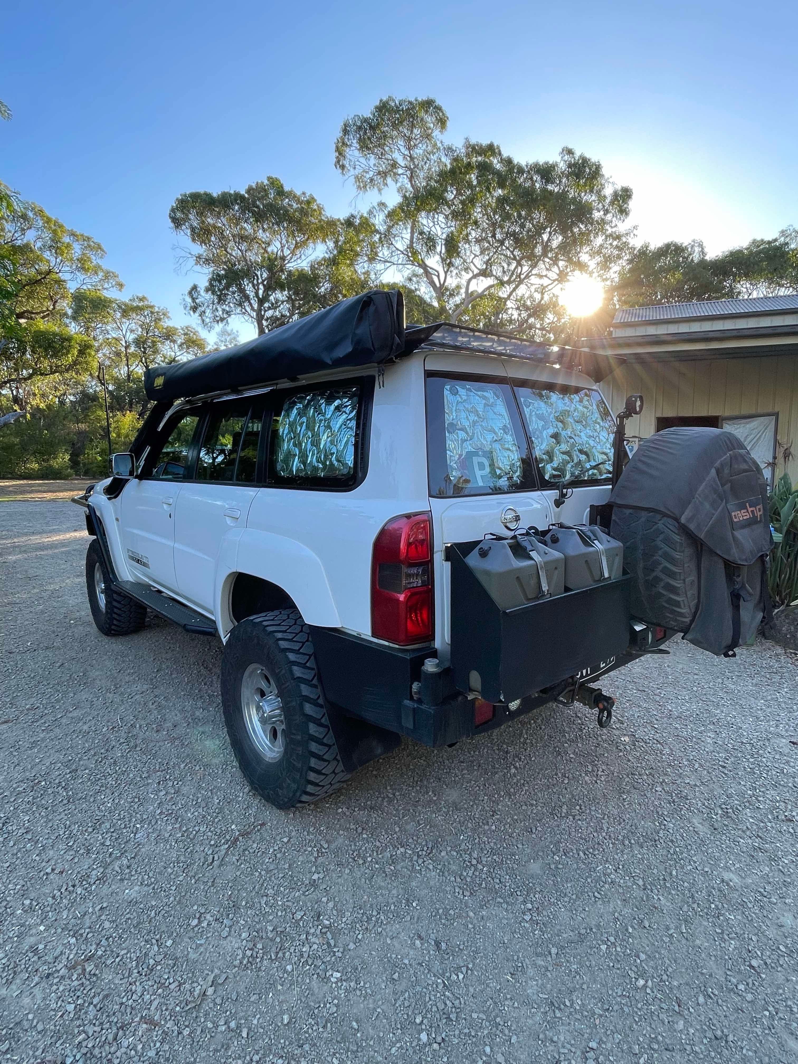 This is an image of a white Nissan Patrol 4x4 with Tier One Metalworks roof racks and rear bar fitted, parked outdoors