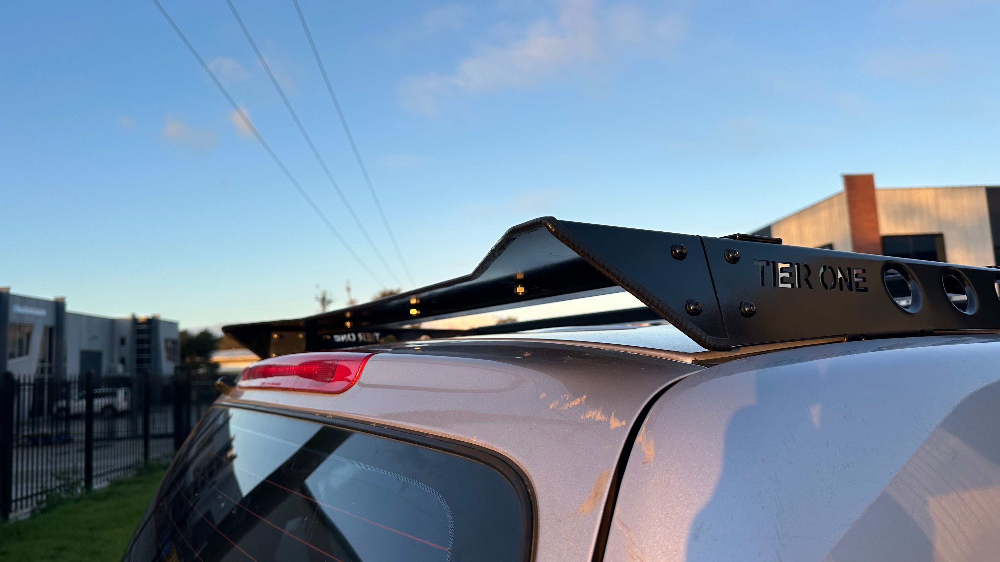 This is an image of a silver vehicle fitted with a black Tier One Metalworks roof rack mounted on the roof in an outdoor industrial area