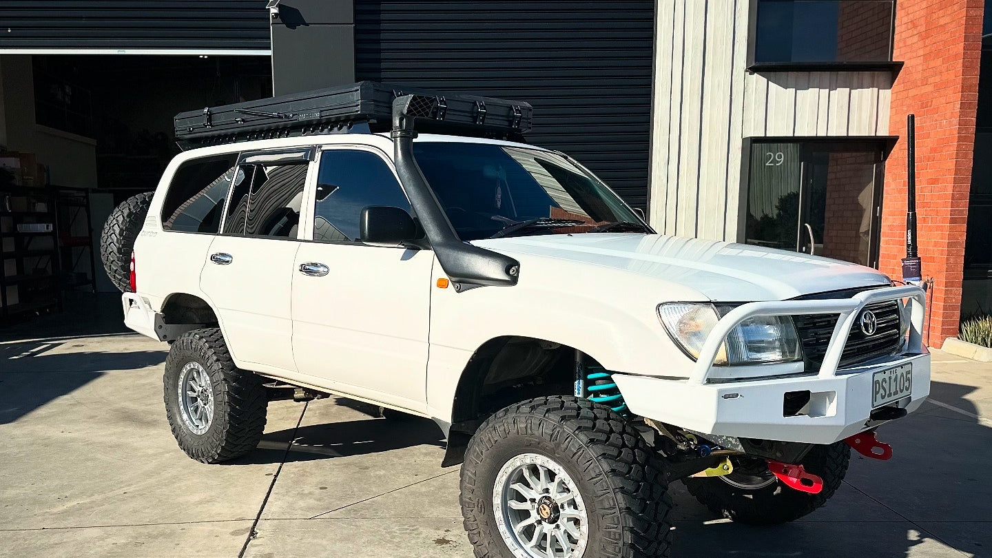 This is an image of a white Toyota Land Cruiser with Tier One Metalworks Roof Rack & Rails, snorkel, bull bar, and off-road tyres outside a workshop.