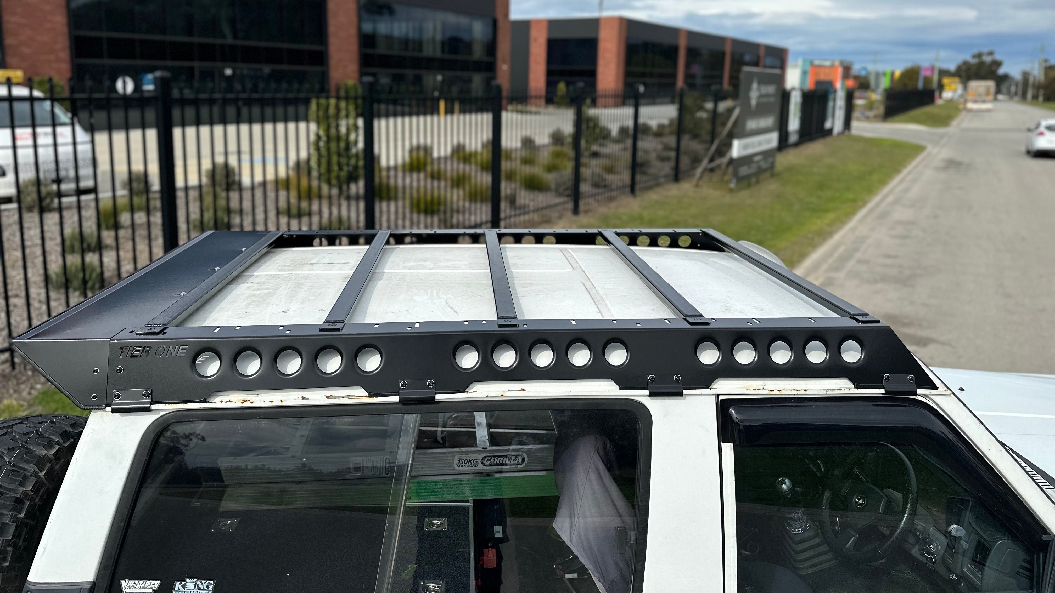 This is an image of a white 4x4 with a Tier One Metalworks black roof rack installed in an industrial area in Australia