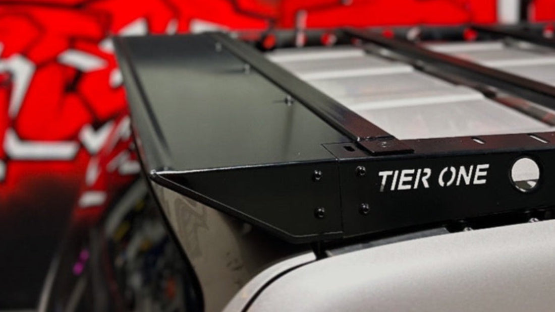 This is an image of a black Tier One Metalworks roof rack mounted on a silver vehicle with a red and black background.