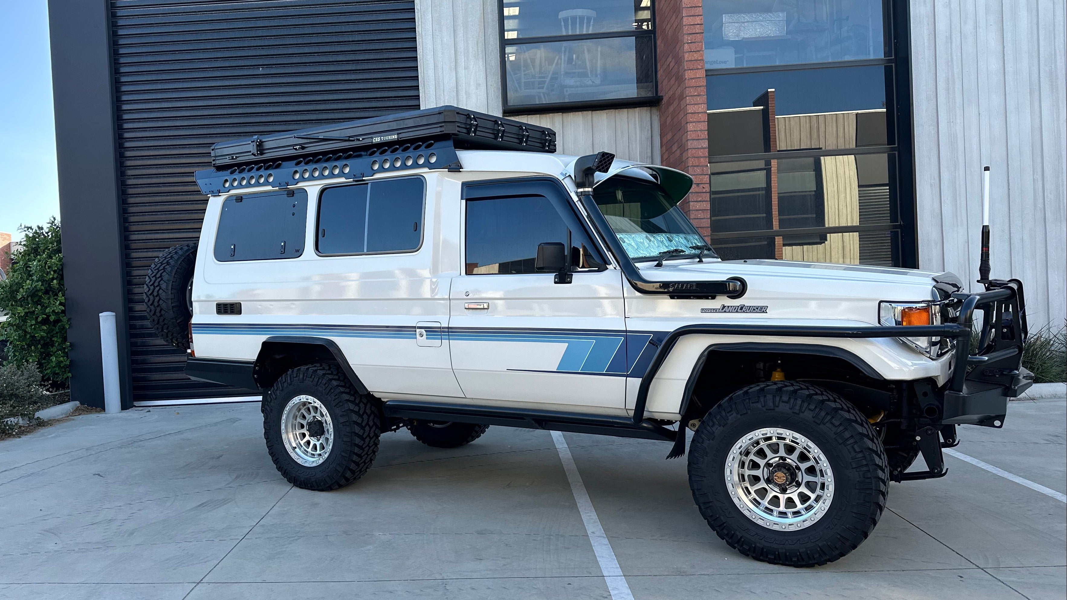 This is an image of a white Toyota Land Cruiser 70 Series fitted with Tier One Metalworks Roof Racks & Rails and off-road accessories in an industrial setting