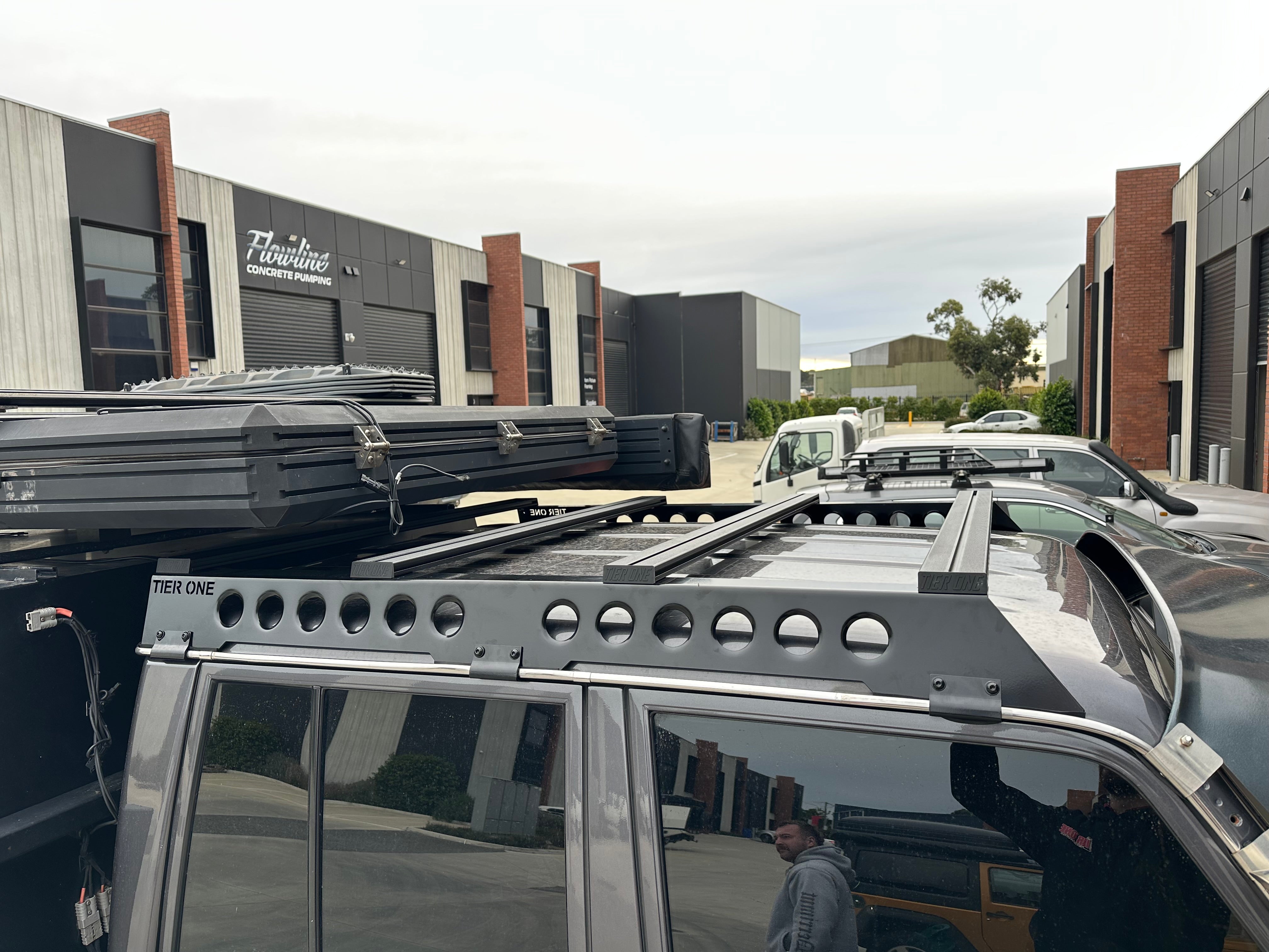 This is an image of a black 4x4 vehicle equipped with Tier One Metalworks black roof racks and rails in an industrial area.