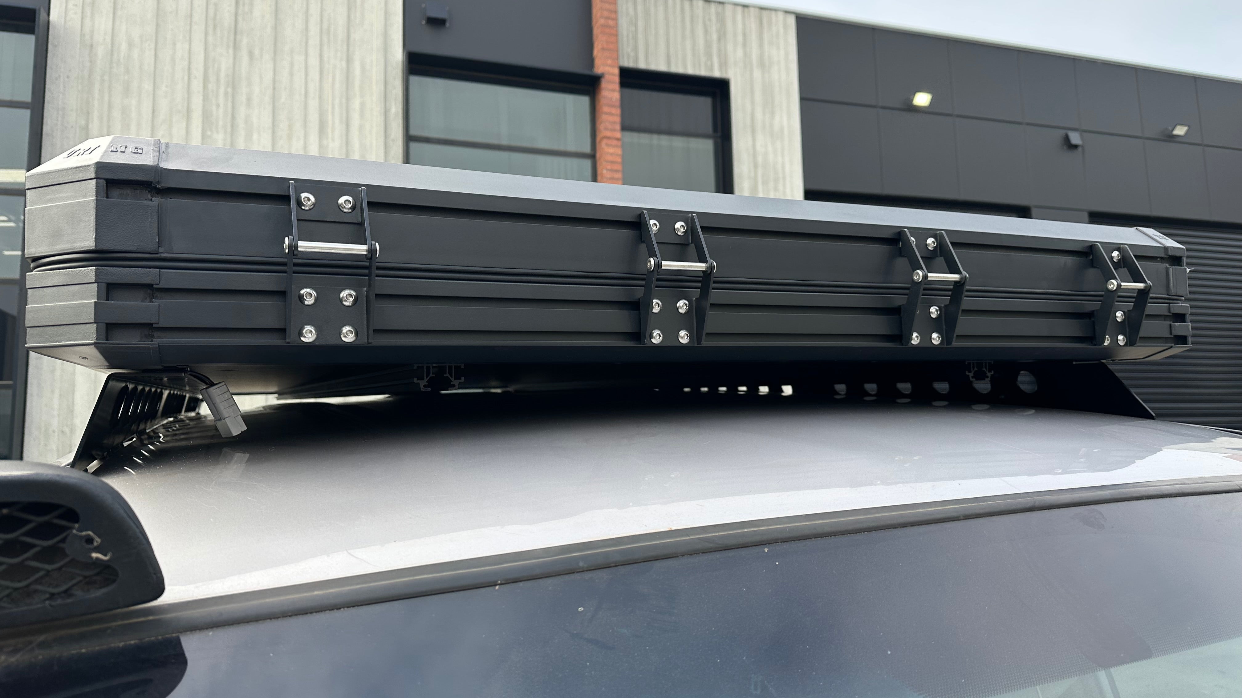 This is an image of a black rooftop tent mounted on a silver vehicle with a Tier One Metalworks roof rack in an industrial setting