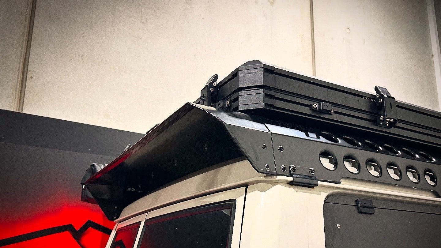 This is an image of a white 4x4 vehicle equipped with a black Tier One Metalworks Roof Rack and Rails in a garage with red wall art.